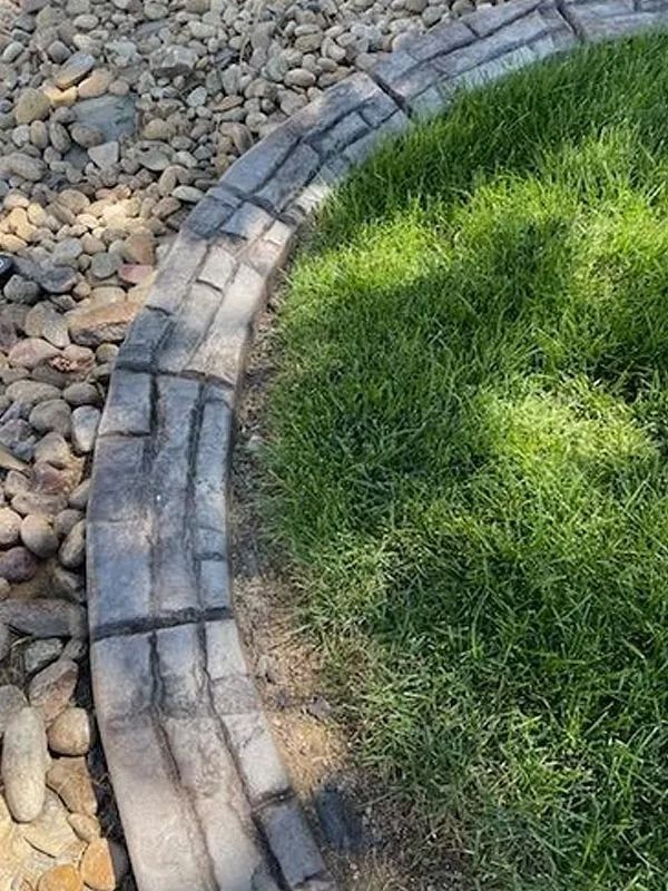 Curved stone garden border separating green grass from a bed of gray pebbles
