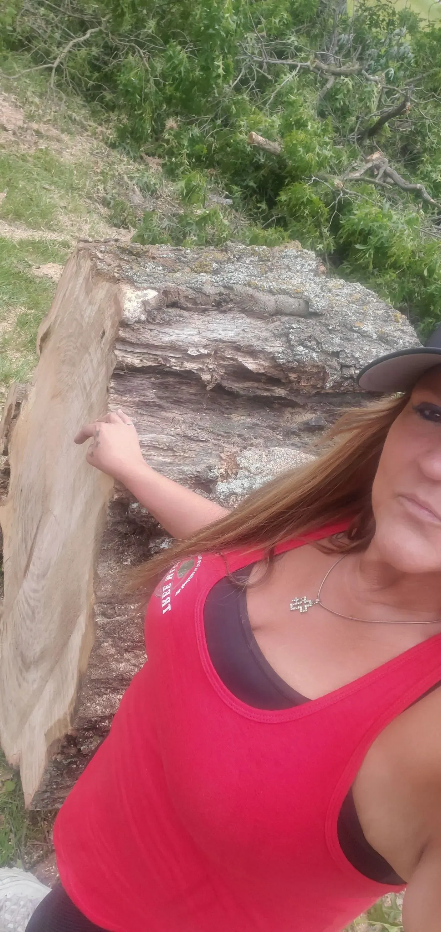 Person in a bright pink top taking a selfie outdoors by a rocky, grassy hillside.