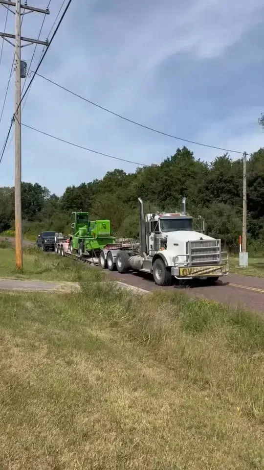 Tow truck hauling a vehicle along a rural road beside a utility pole and grassy shoulder.