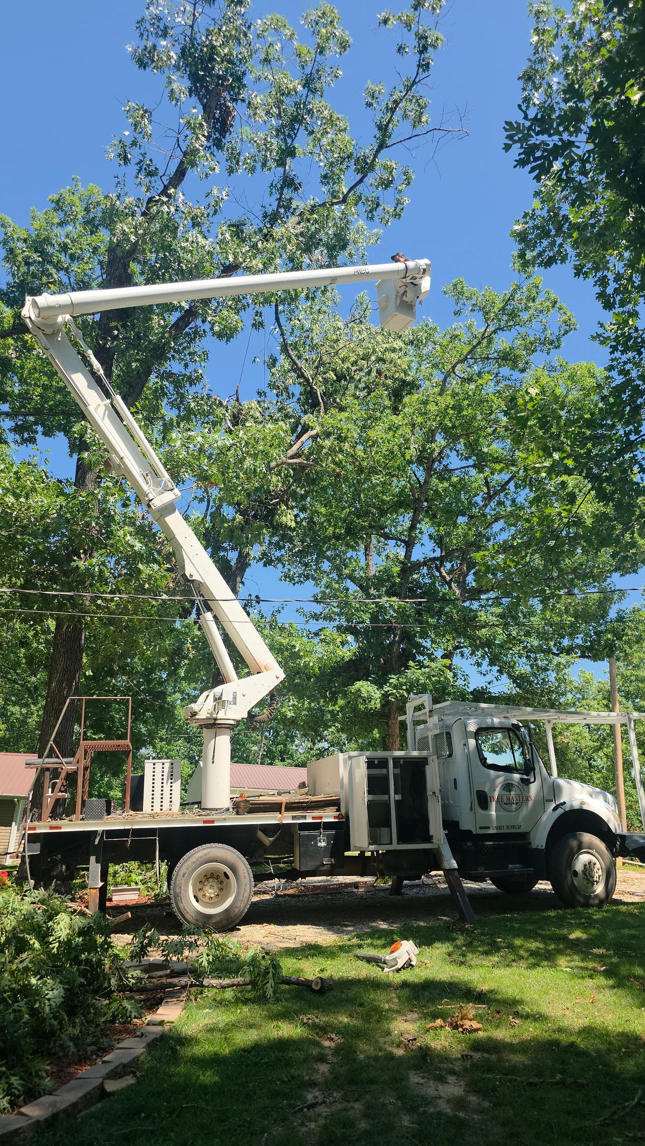 White boom truck raised in a leafy yard under a blue sky