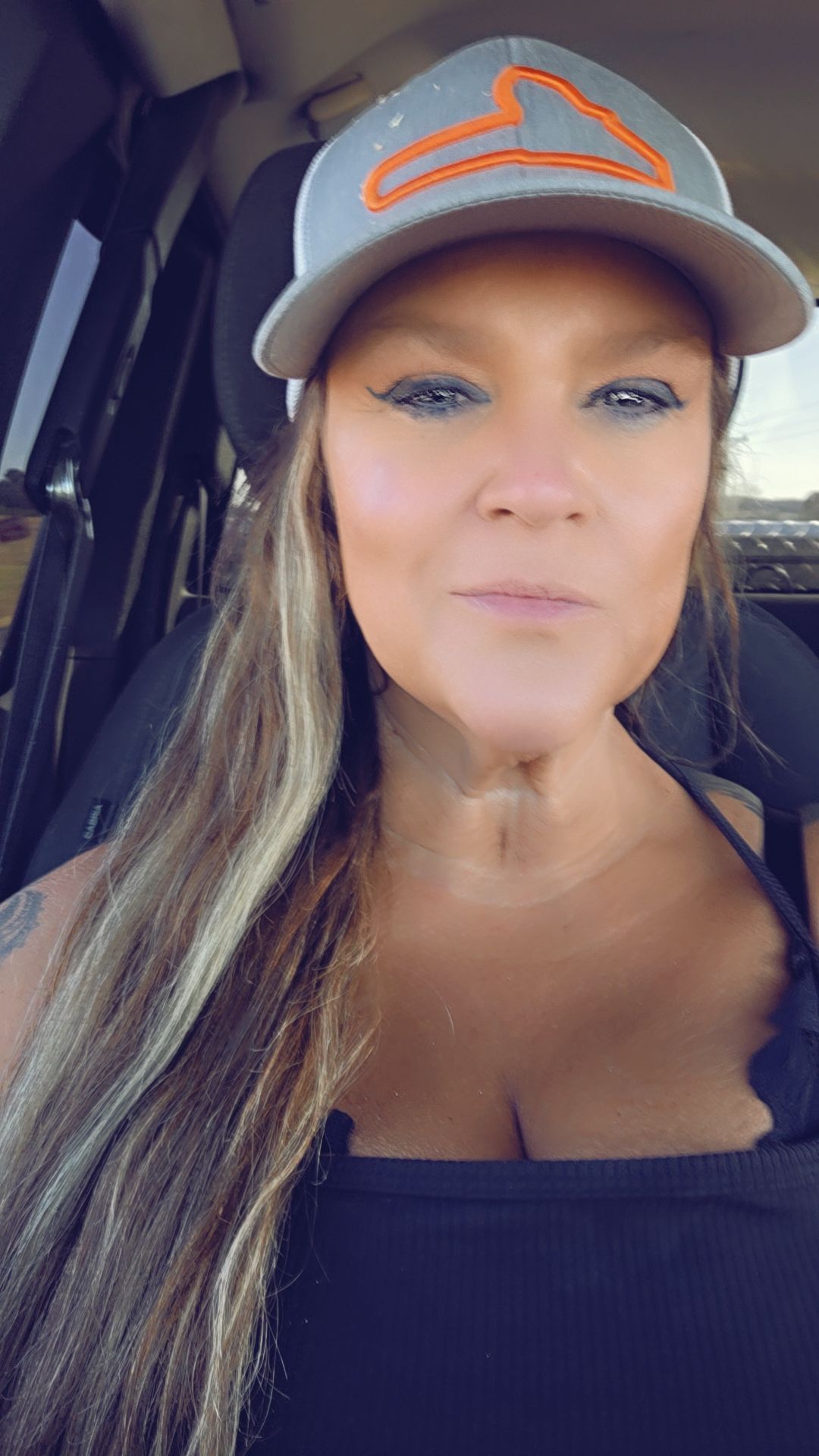 Woman in a gray cap and black top, seated in a car, looking at the camera.