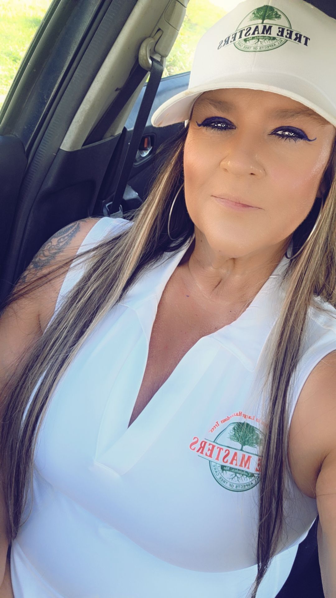 Woman in a white cap and polo shirt taking a selfie in a car.