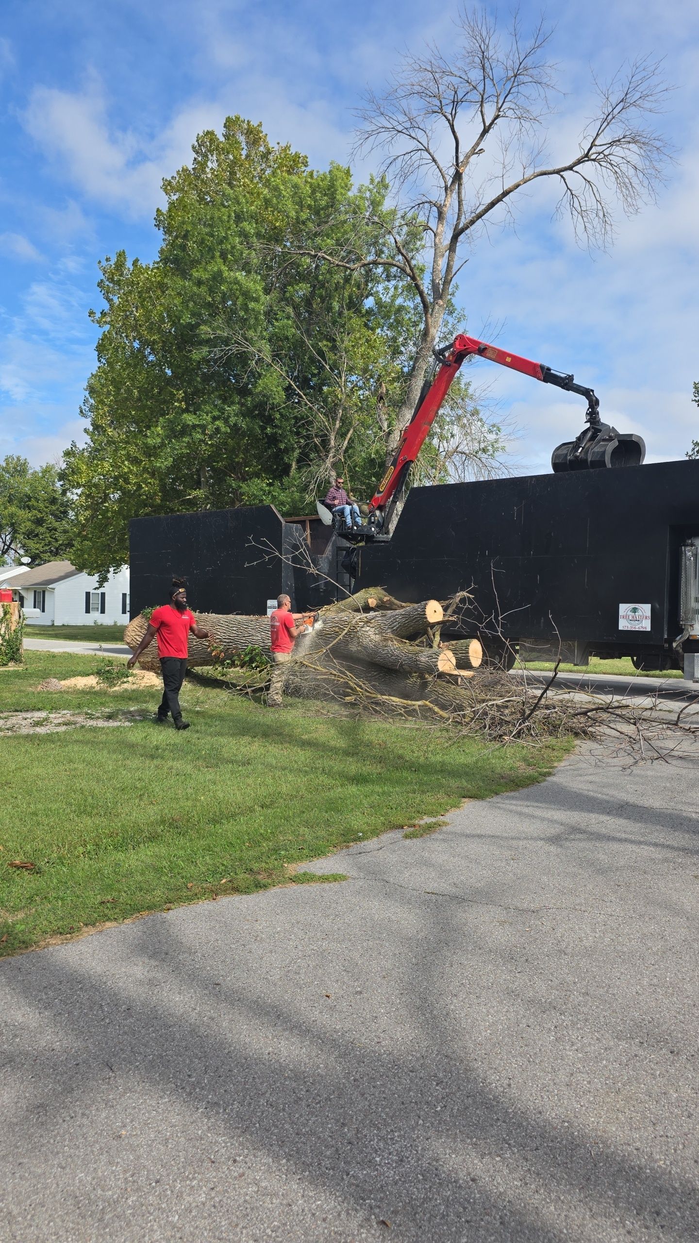 Workers using a red excavator beside a black truck on a residential street under a blue sky