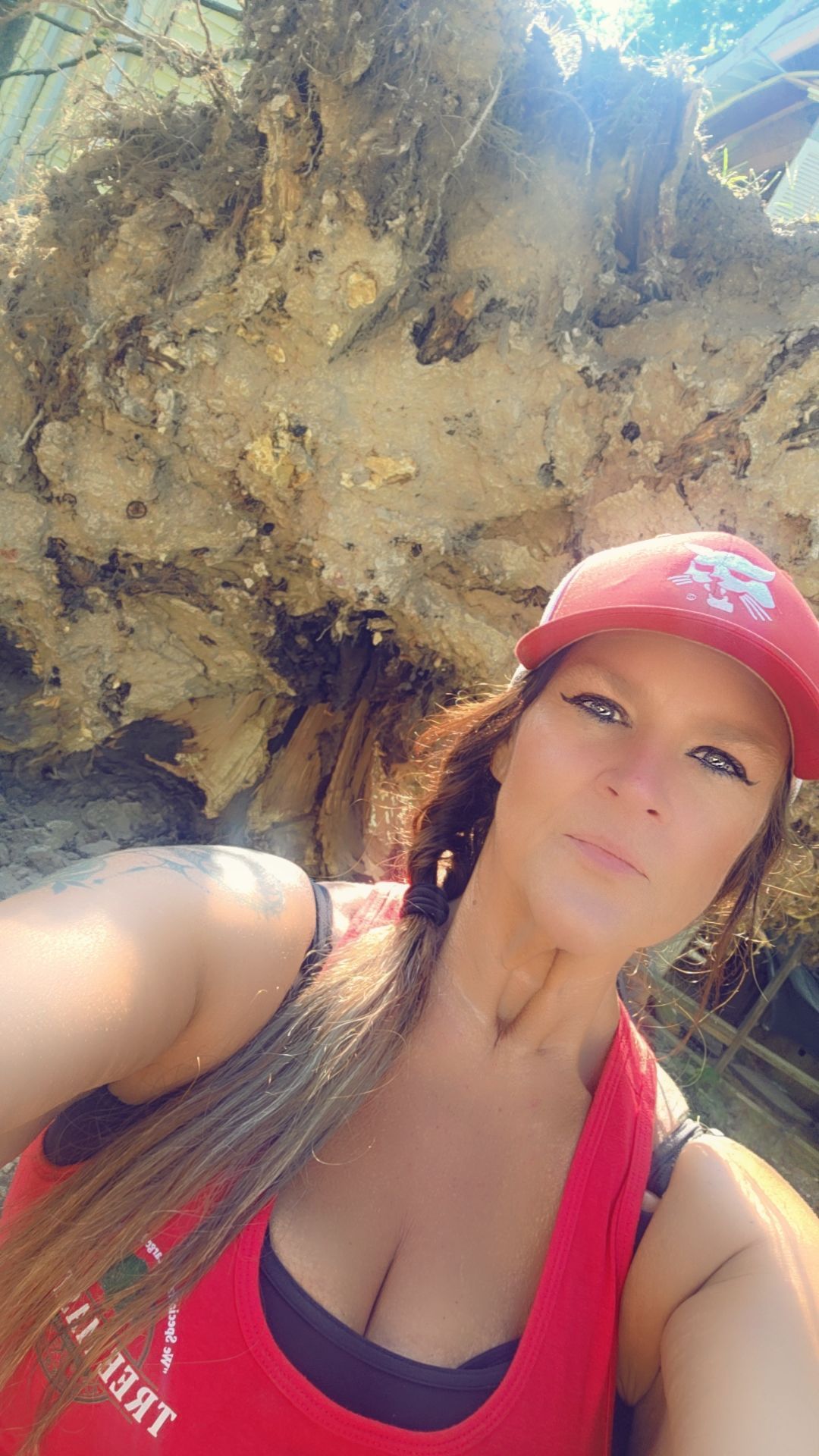 Woman in a red cap and tank top taking a selfie outdoors in front of a rocky cliff.