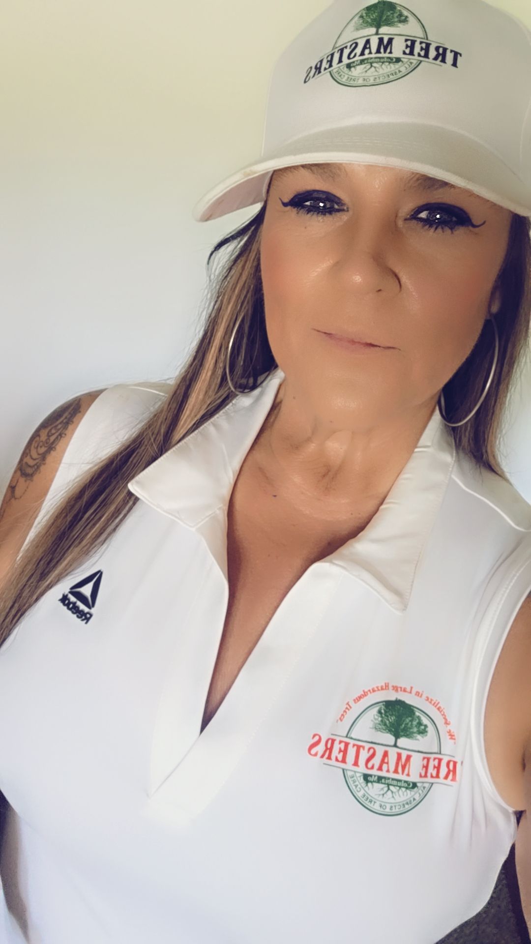 Woman in white baseball cap and polo shirt with logo, posing indoors against a plain background.