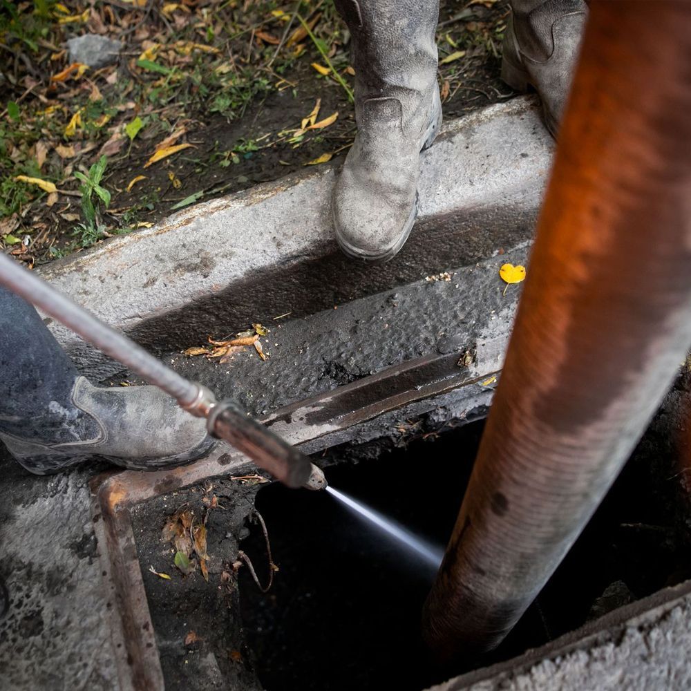 A person is using a hydro jet to clean a drain