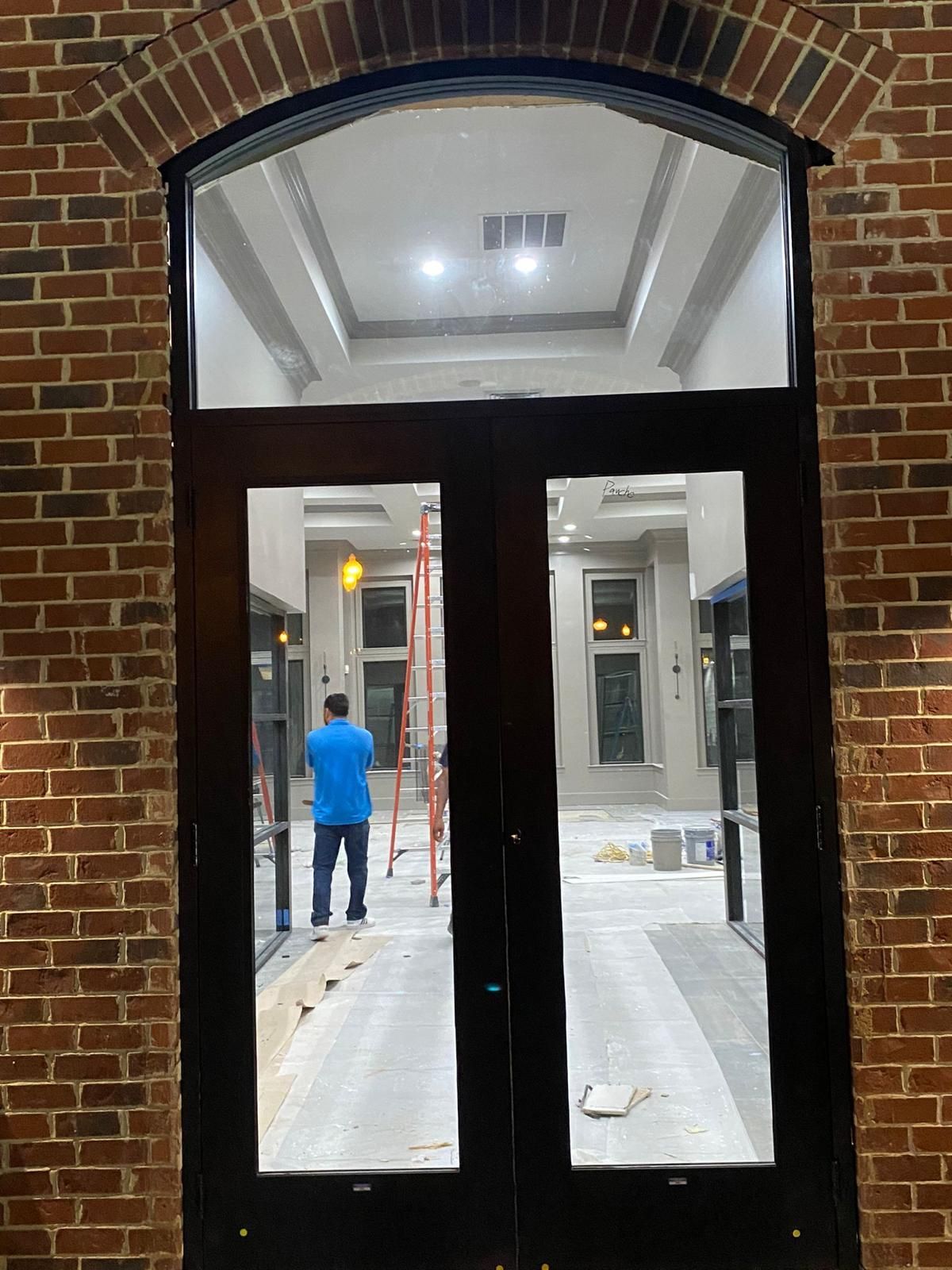 A man in a blue shirt is standing in front of a large glass door.