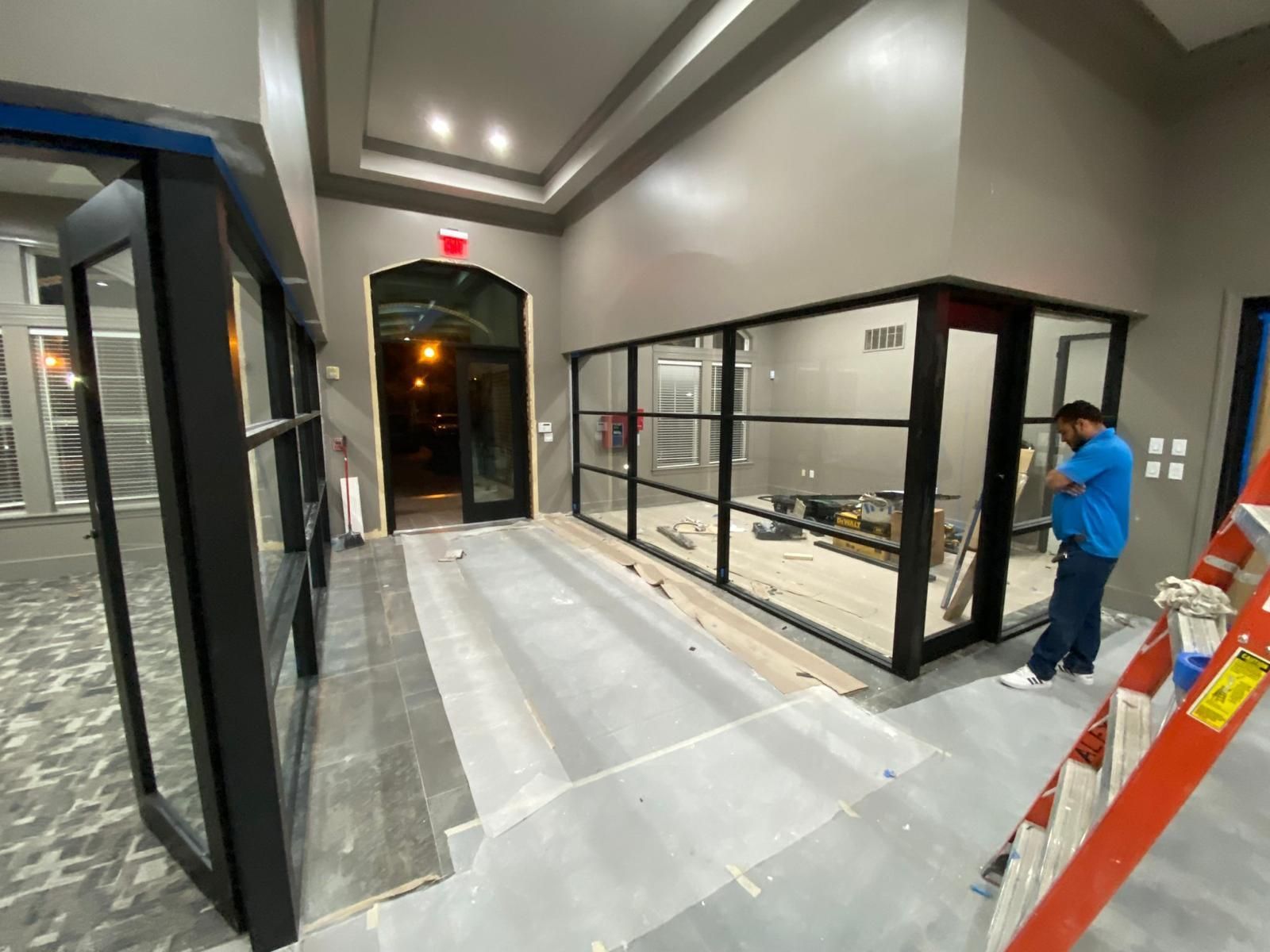 A man is standing on a ladder in a room with a lot of windows.