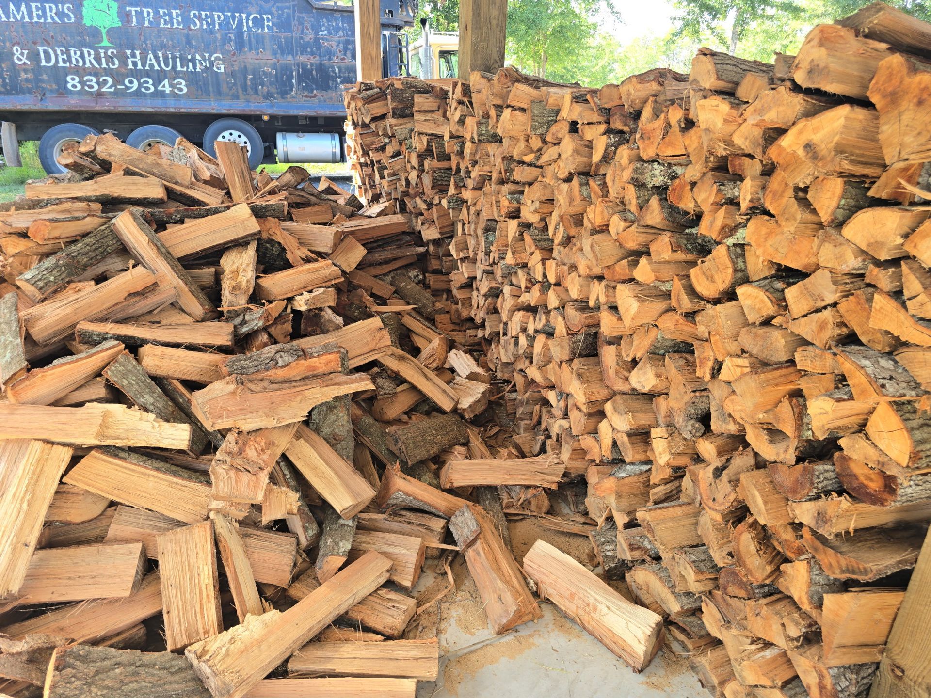 Stacks of split firewood piled outdoors beside a truck.