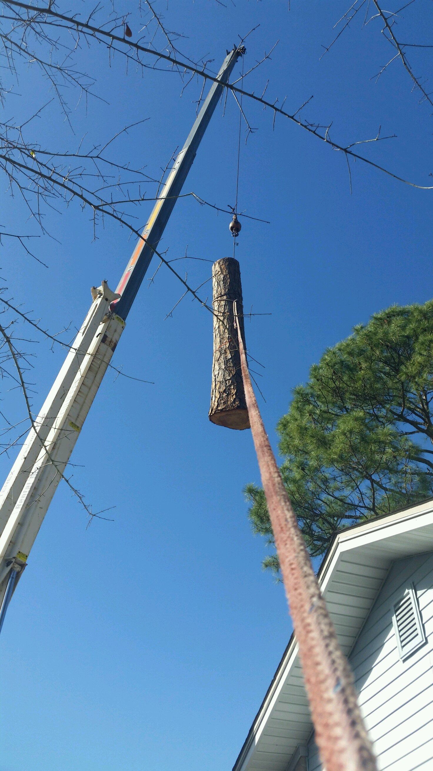 Crane lifting a long wrapped object beside a house under a clear blue sky