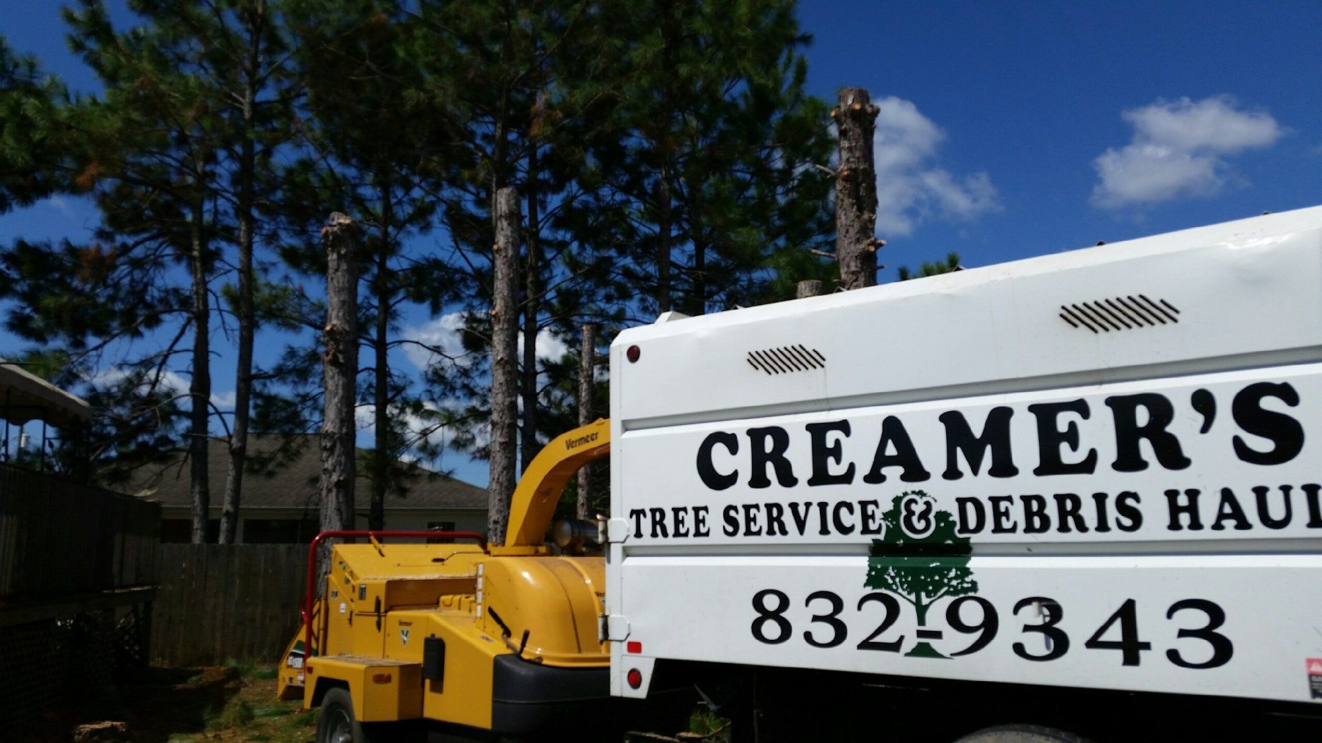 Creamer’s tree service truck with crane and debris hauler parked among tall trees outdoors