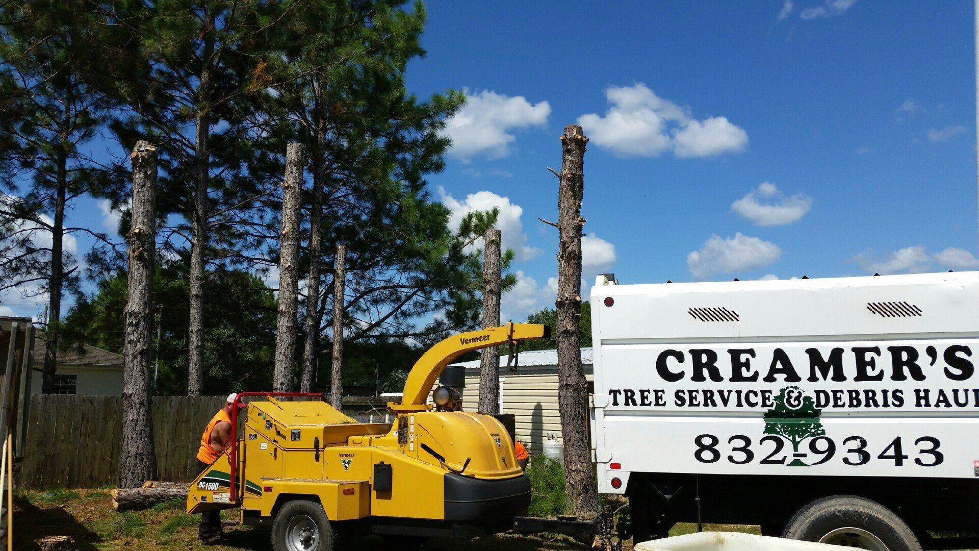 Yellow wood chipper beside a white Creemer’s tree service truck outdoors under a blue sky