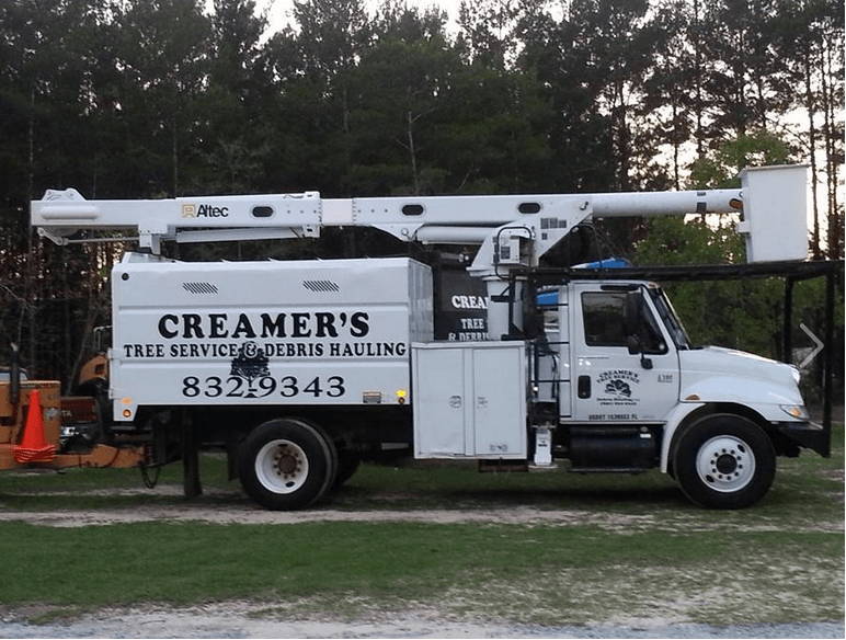 White tree service truck with “Cremers” signage and boom lift parked outdoors near trees