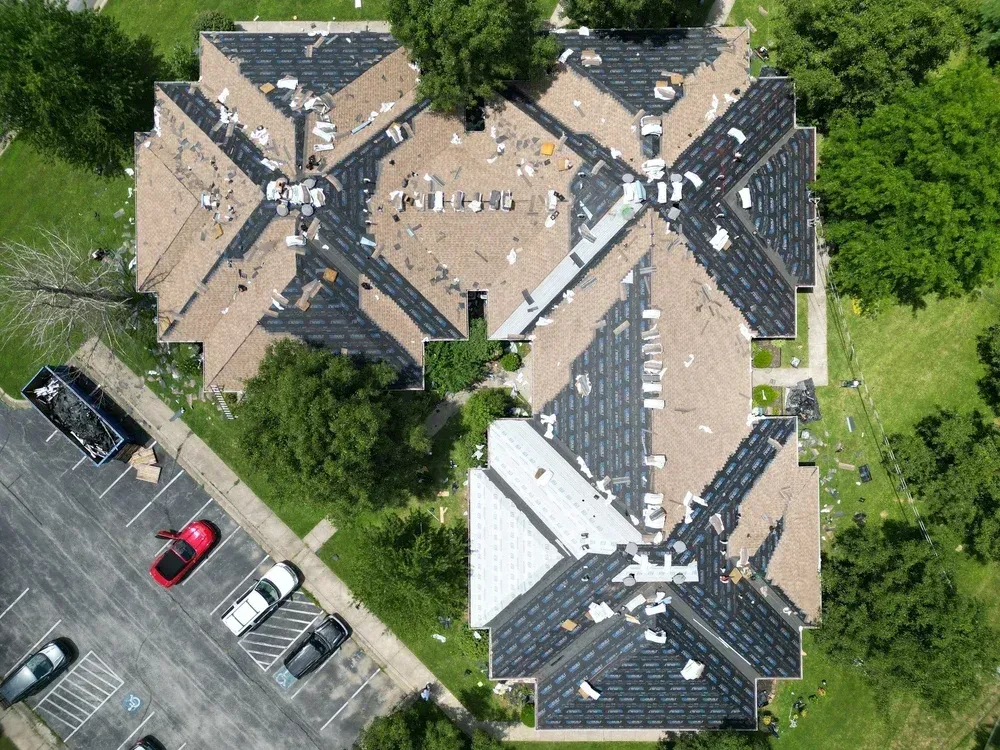 Aerial view of two tan-roofed buildings beside a parking lot and trees