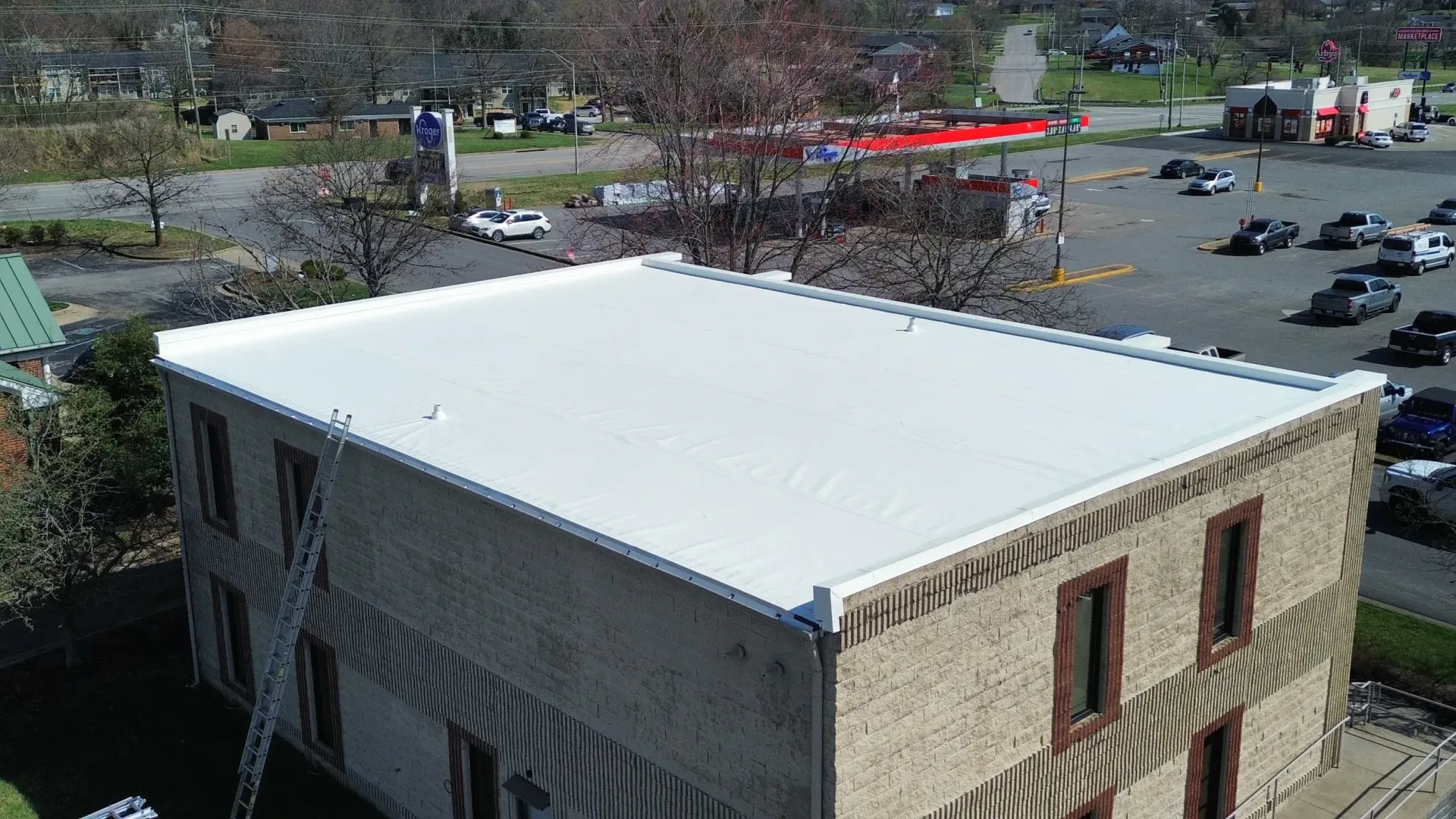 Aerial view of a building with a white roof beside a parking lot and trees