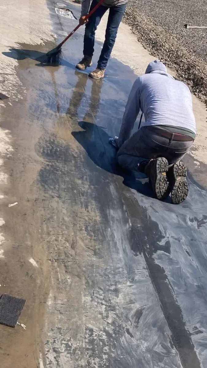Two workers patching a pothole on a wet road, one kneeling and one using a shovel
