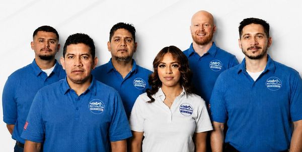 Six employees pose against a white background, wearing blue and white company shirts.