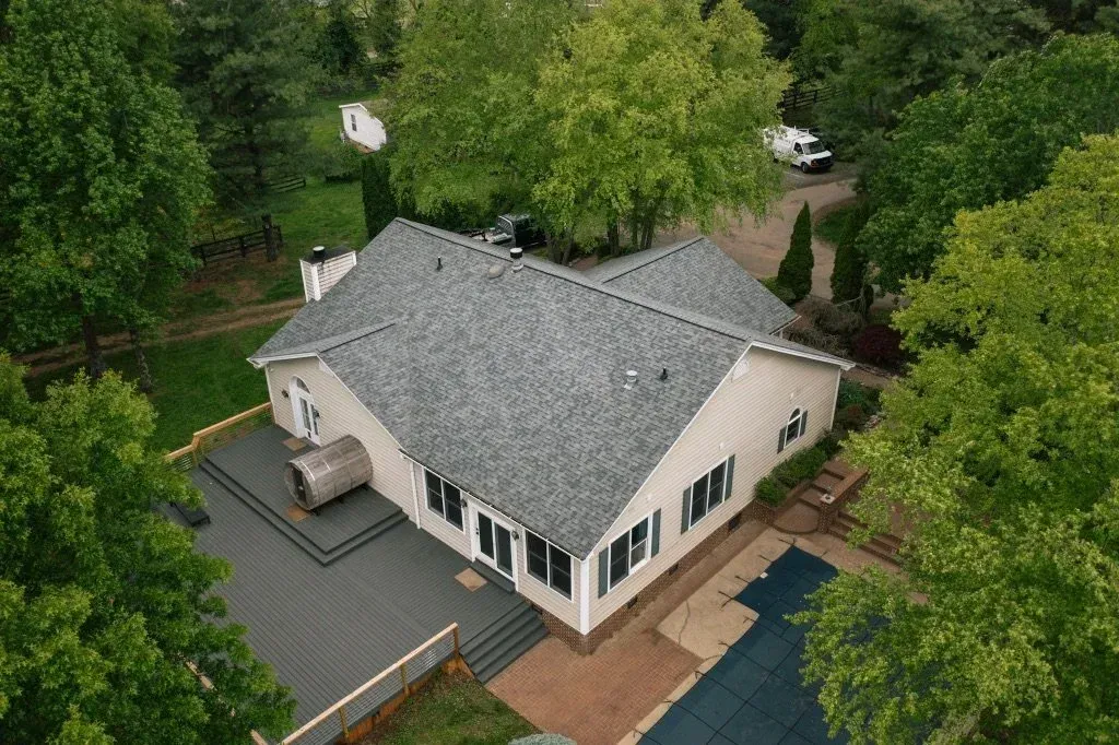 Aerial view of a white house with a gray roof, surrounded by green trees and a driveway.