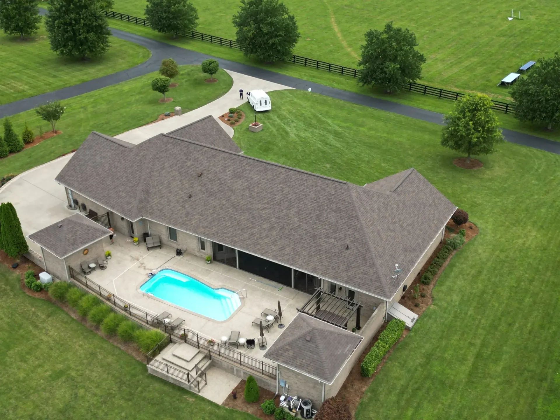 Aerial view of a suburban house with a backyard pool, patio furniture, and green lawn.