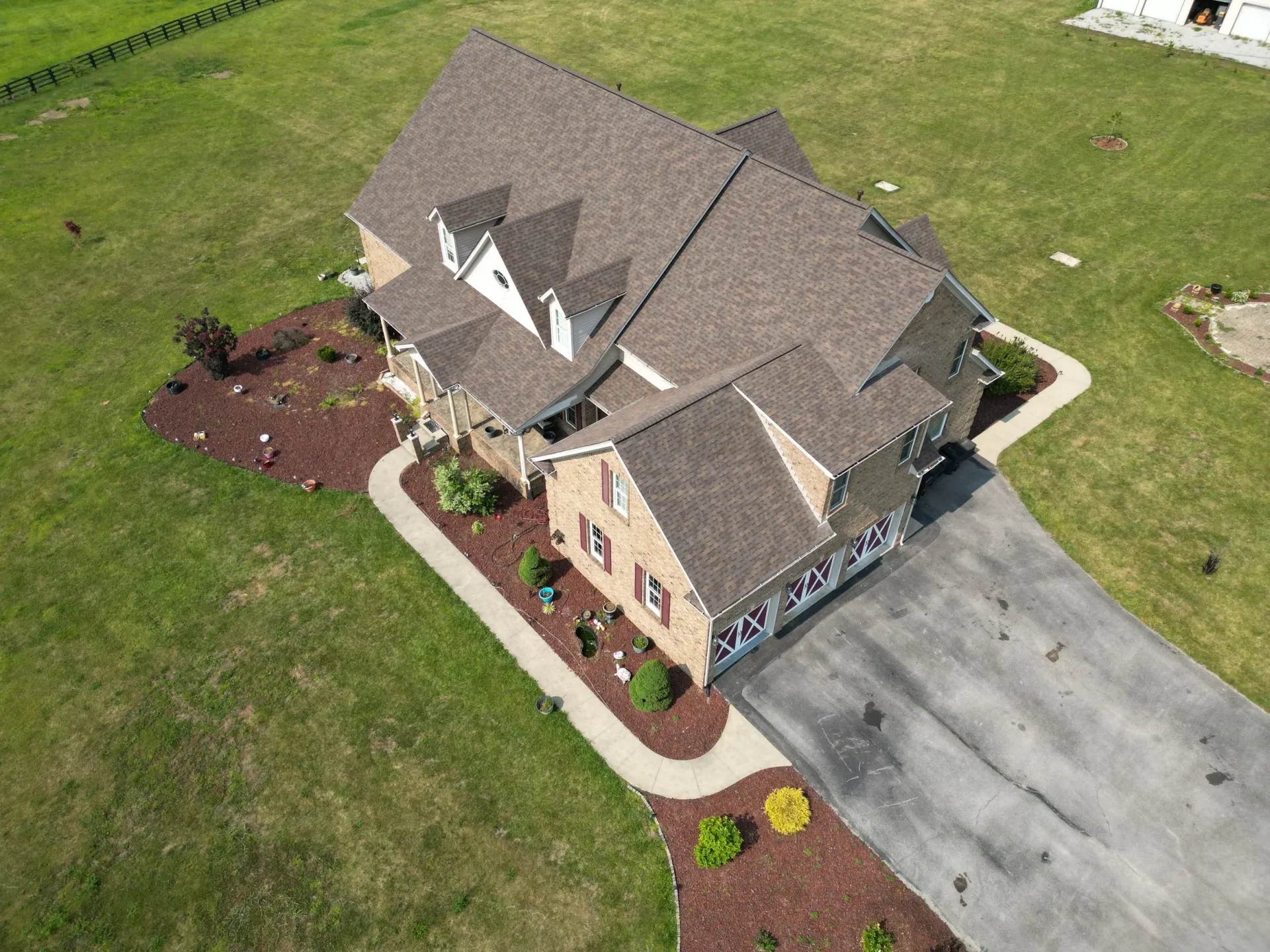 Aerial view of a brick house with a driveway, landscaped front yard, and surrounding lawn.