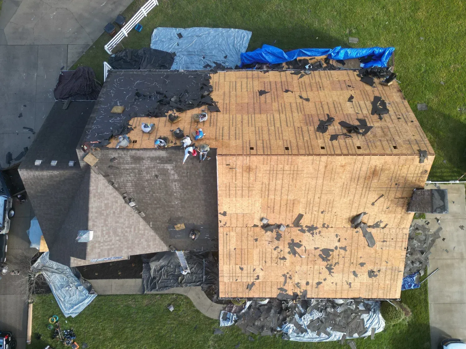 Aerial view of a house roof with tarp-covered damaged sections and debris scattered around.