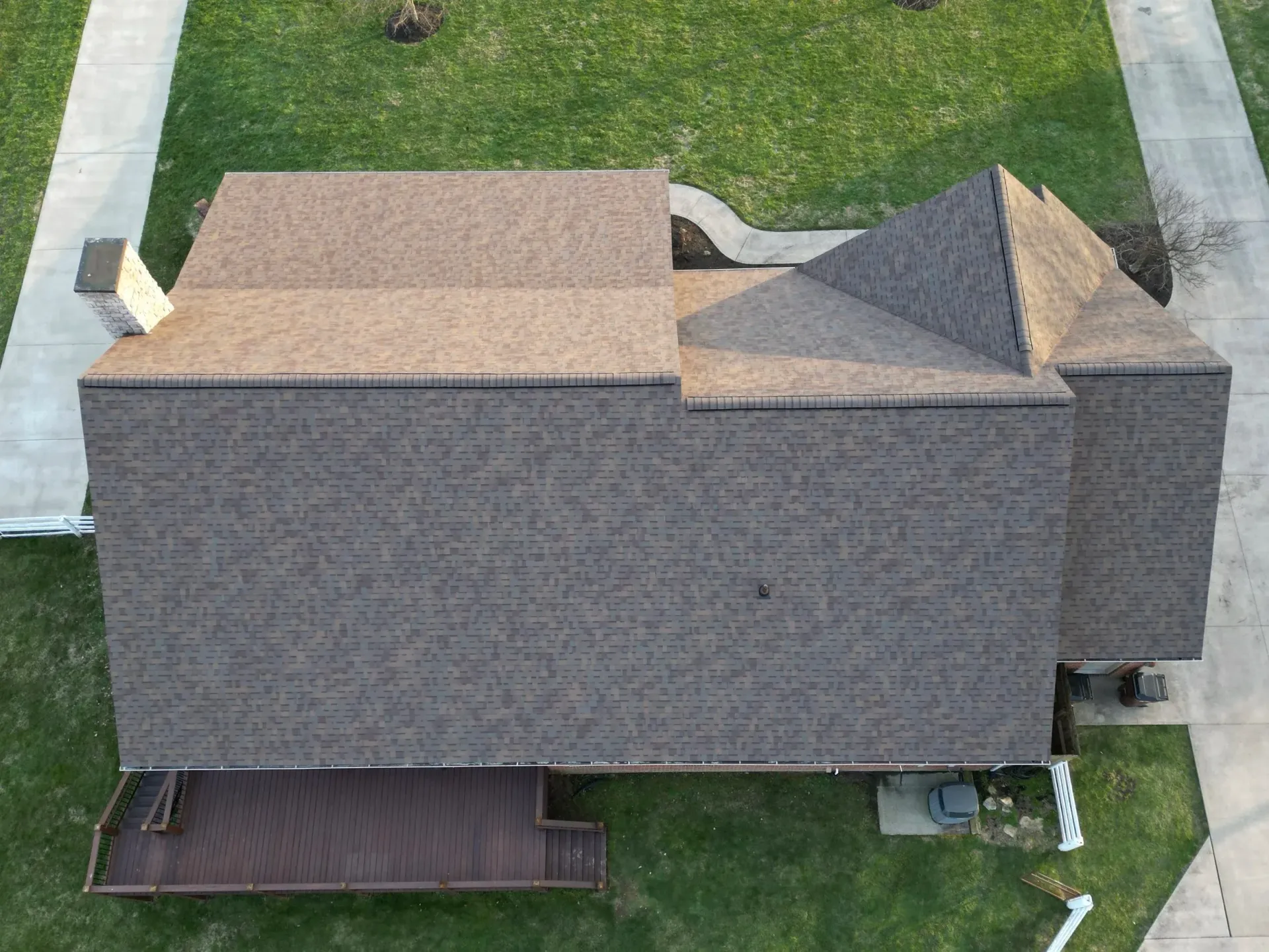 Aerial view of a brown-shingled house with multiple roof sections and a small front porch on a grassy lot