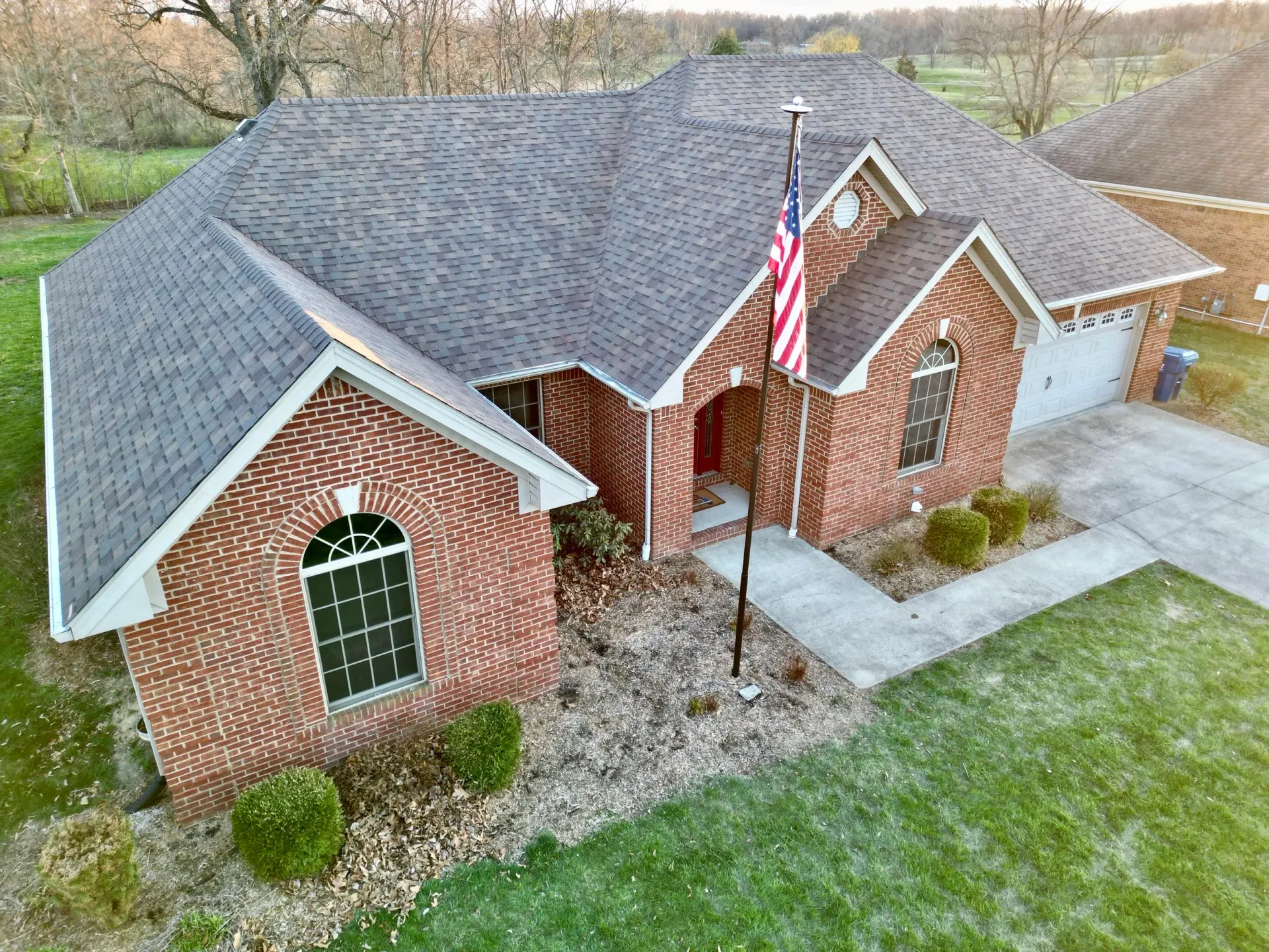 Brick suburban house with gray roof and American flag in the front yard