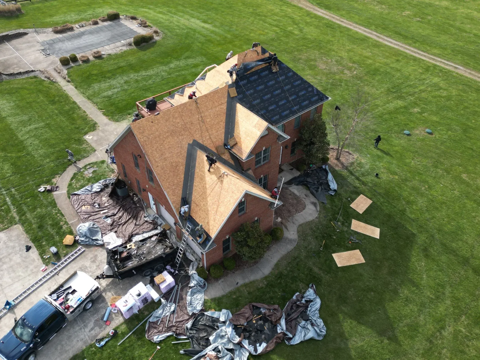Aerial view of a fire-damaged brick house with debris scattered around on a grassy lot.