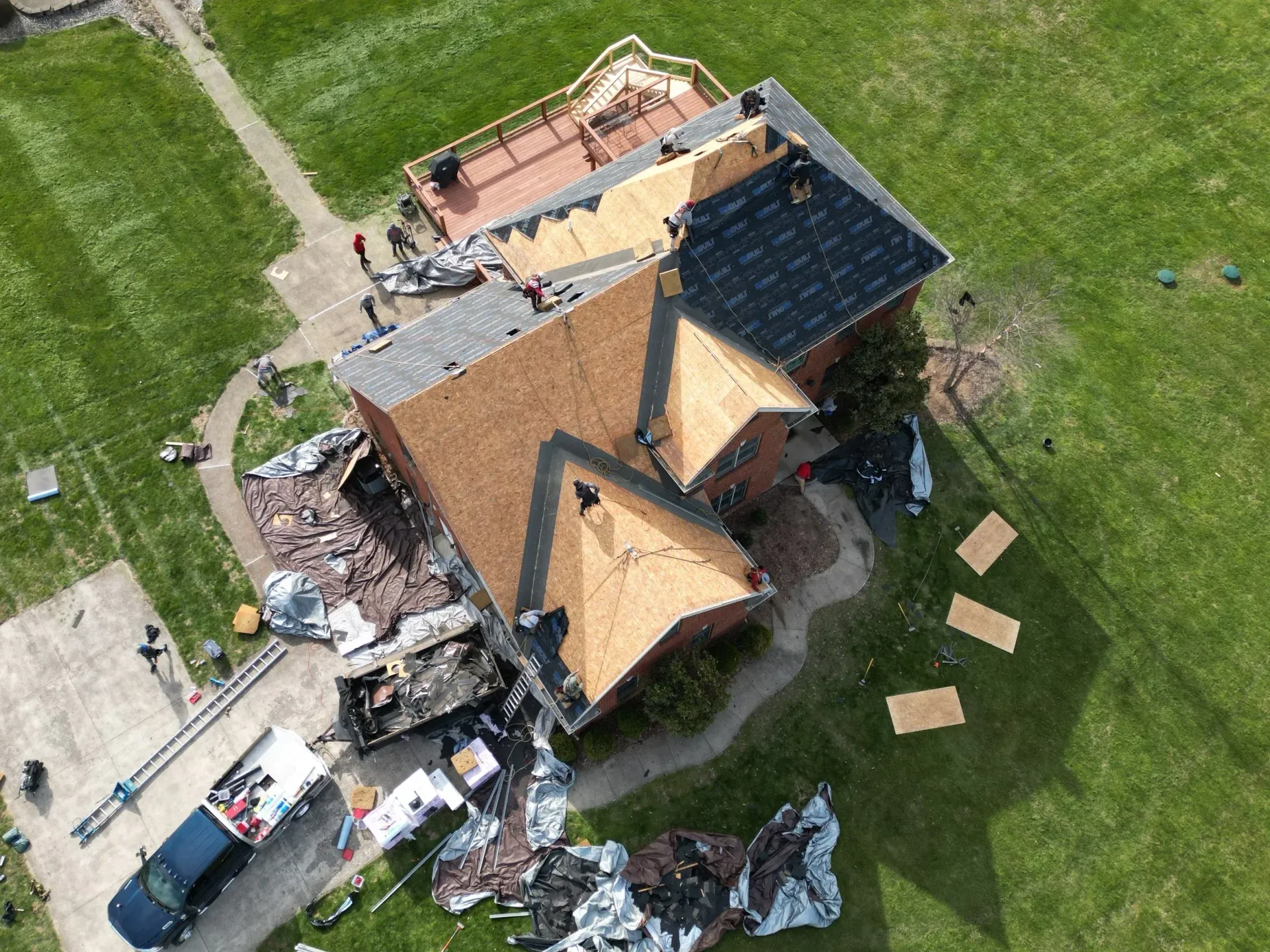 Aerial view of a house with a damaged roof, debris around it, and vehicles parked nearby.