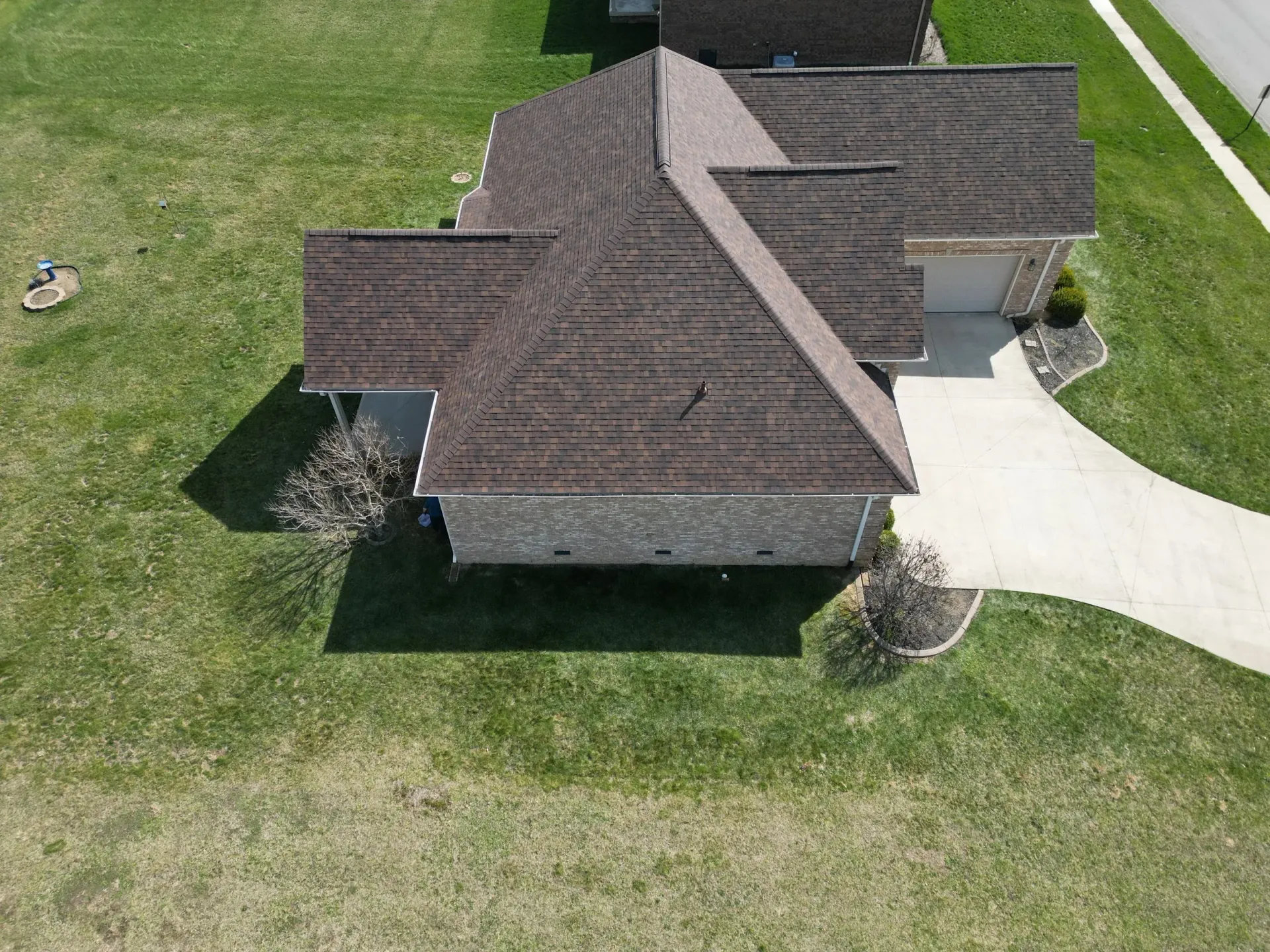 Aerial view of a suburban house with a dark roof, driveway, and surrounding green lawn.