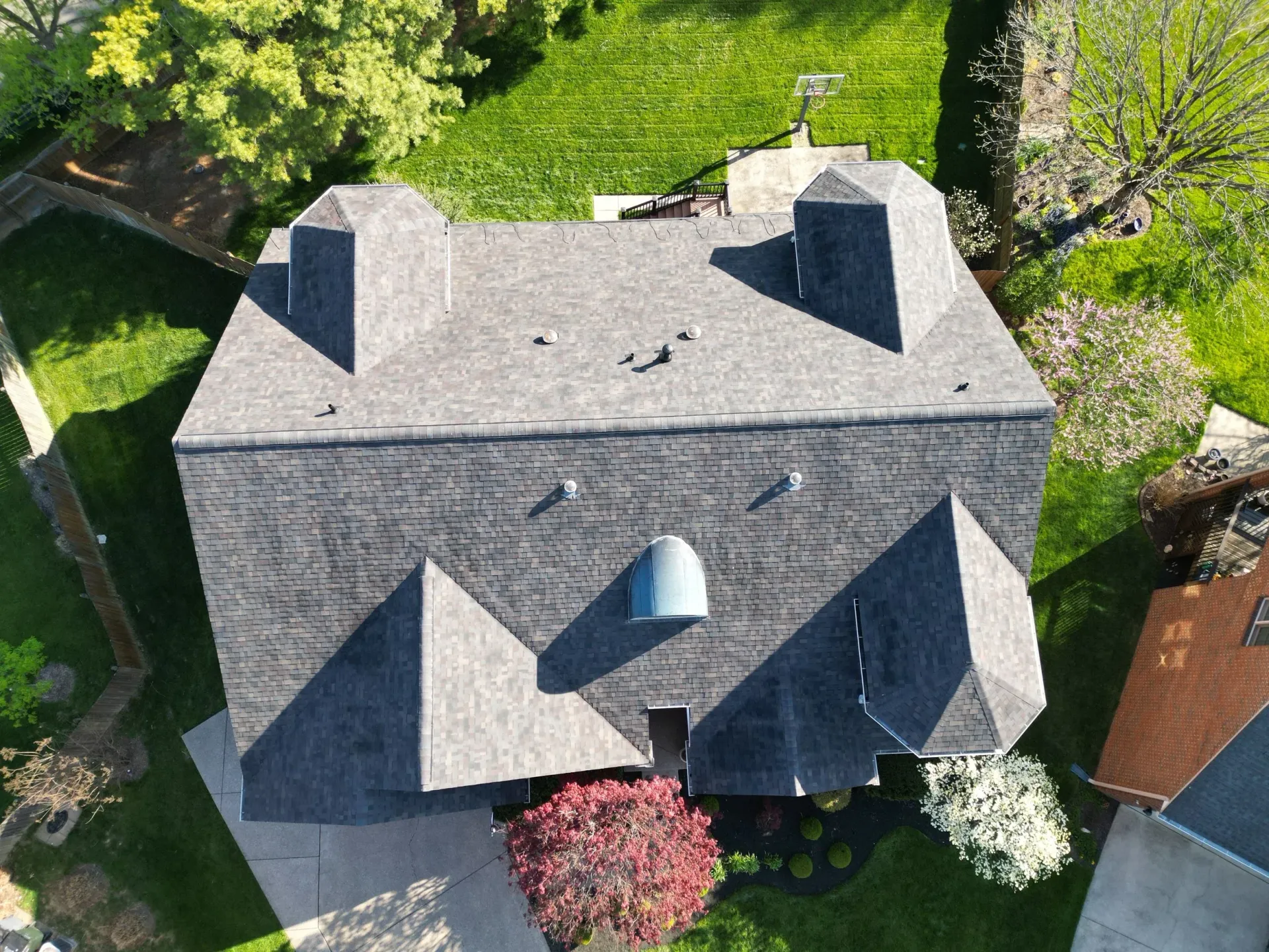 Aerial view of a gray-roofed house surrounded by green trees and shrubs.