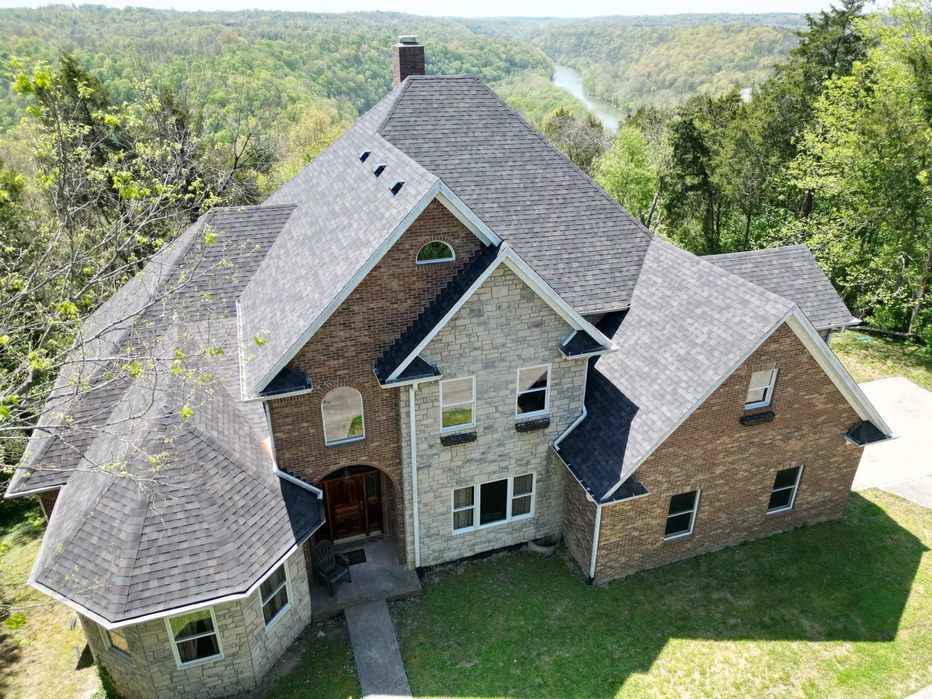 Aerial view of a large brick house with a gray roof surrounded by green trees and lawn.
