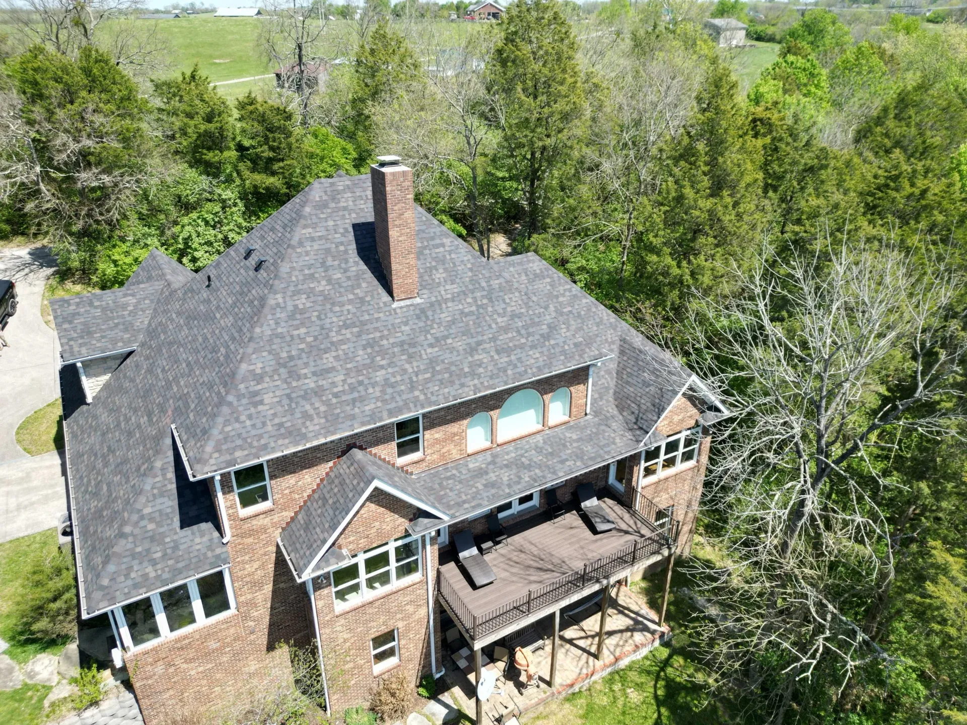 Aerial view of a brick house with a dark gray roof surrounded by trees.