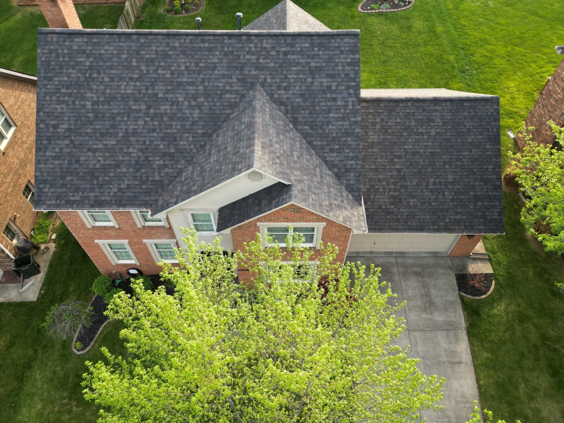 Aerial view of a brick house with a dark shingle roof and green front yard.
