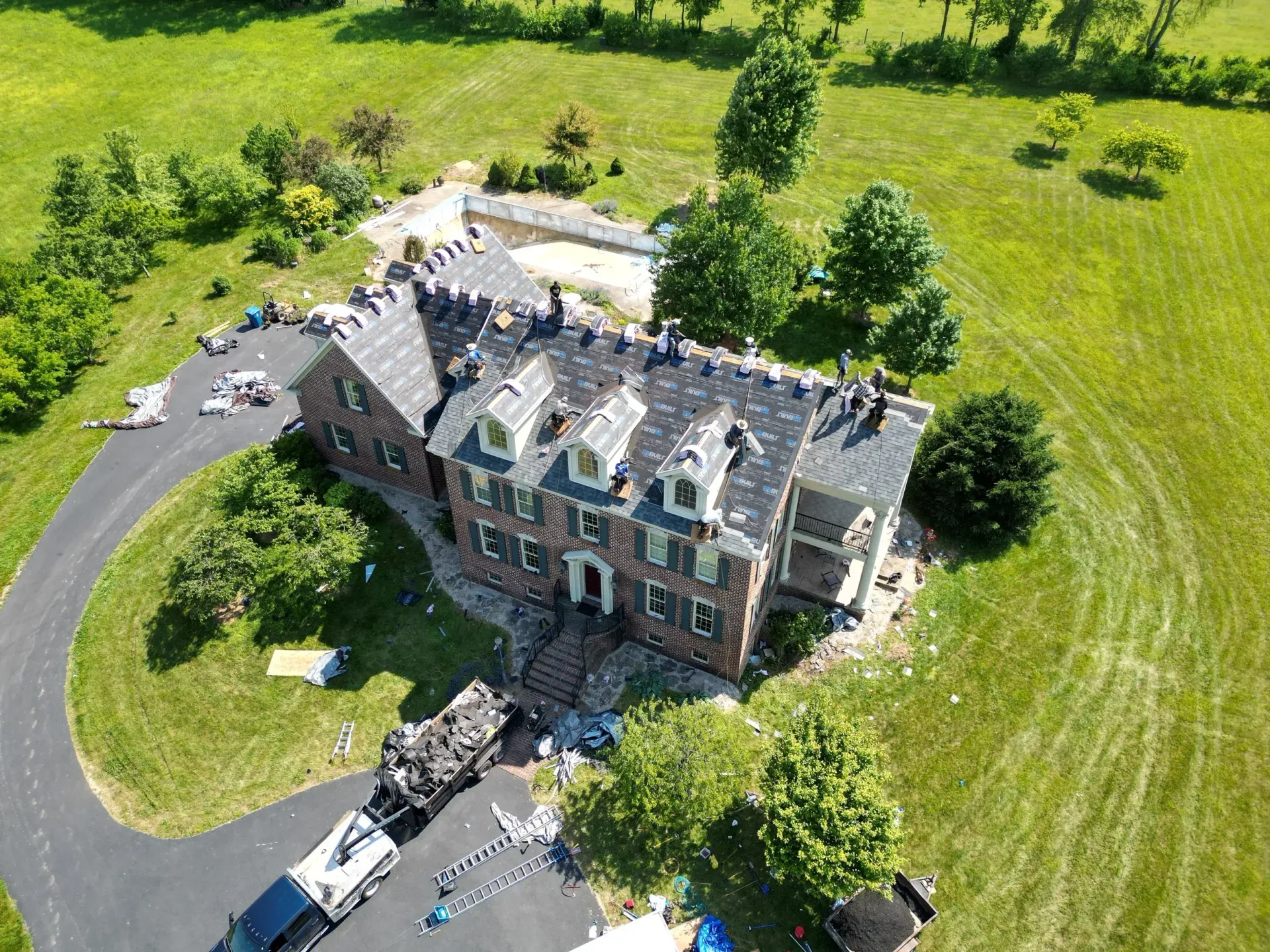 Aerial view of a large stone mansion with a curved driveway, surrounded by bright green fields and trees