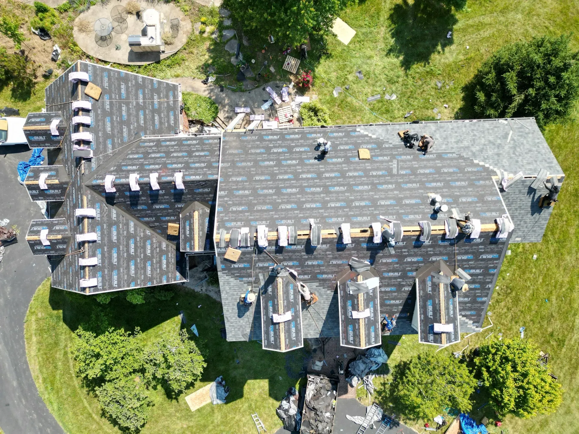 Aerial view of a large stone house with multiple dormers, surrounded by green trees and lawn.