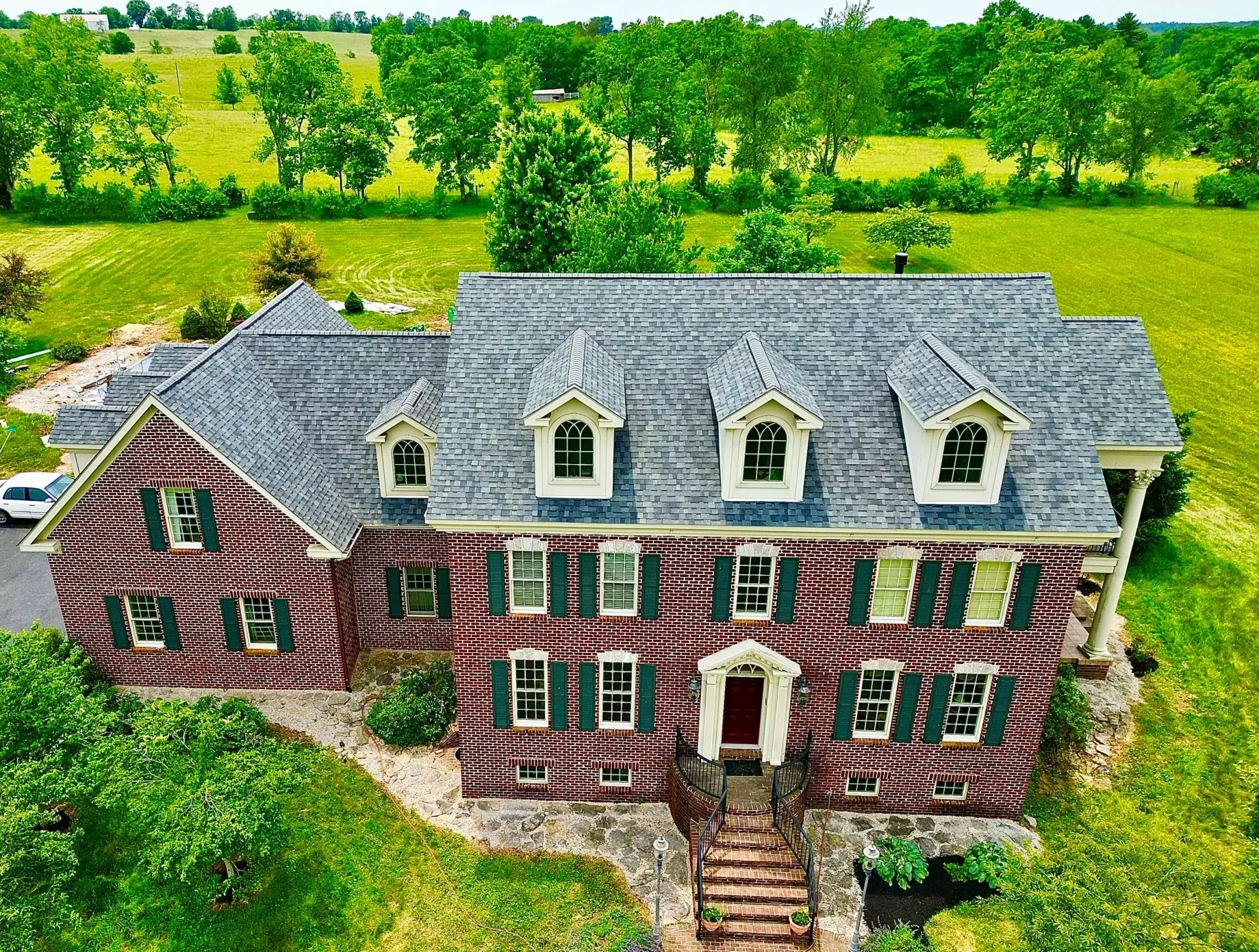 Aerial view of a red brick house with gray roof, surrounded by green fields and trees.