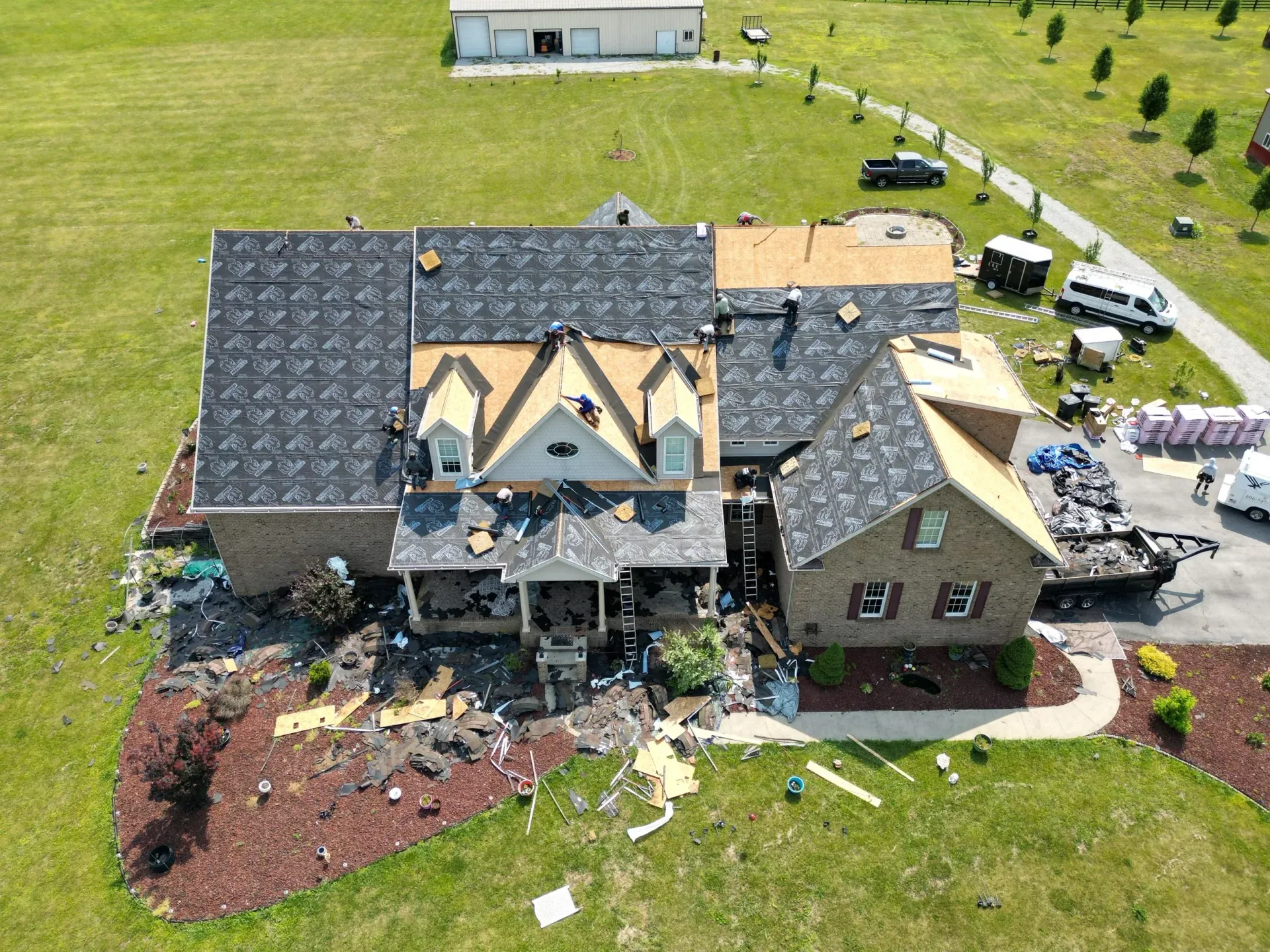 Aerial view of a damaged house with a collapsed roof and debris scattered around the yard.