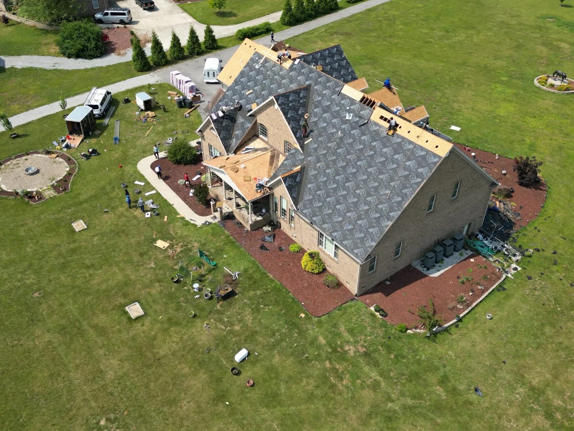 Aerial view of a suburban house with gray roof, tan walls, and a large green lawn.