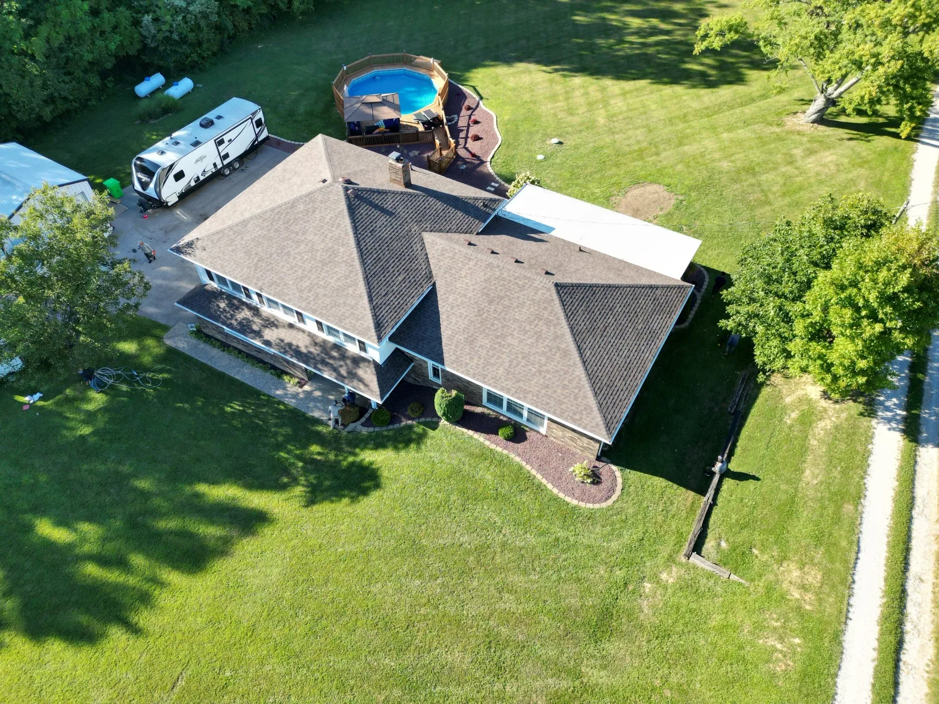Aerial view of a house with a shingled roof, large green lawn, driveway, and a backyard pool.