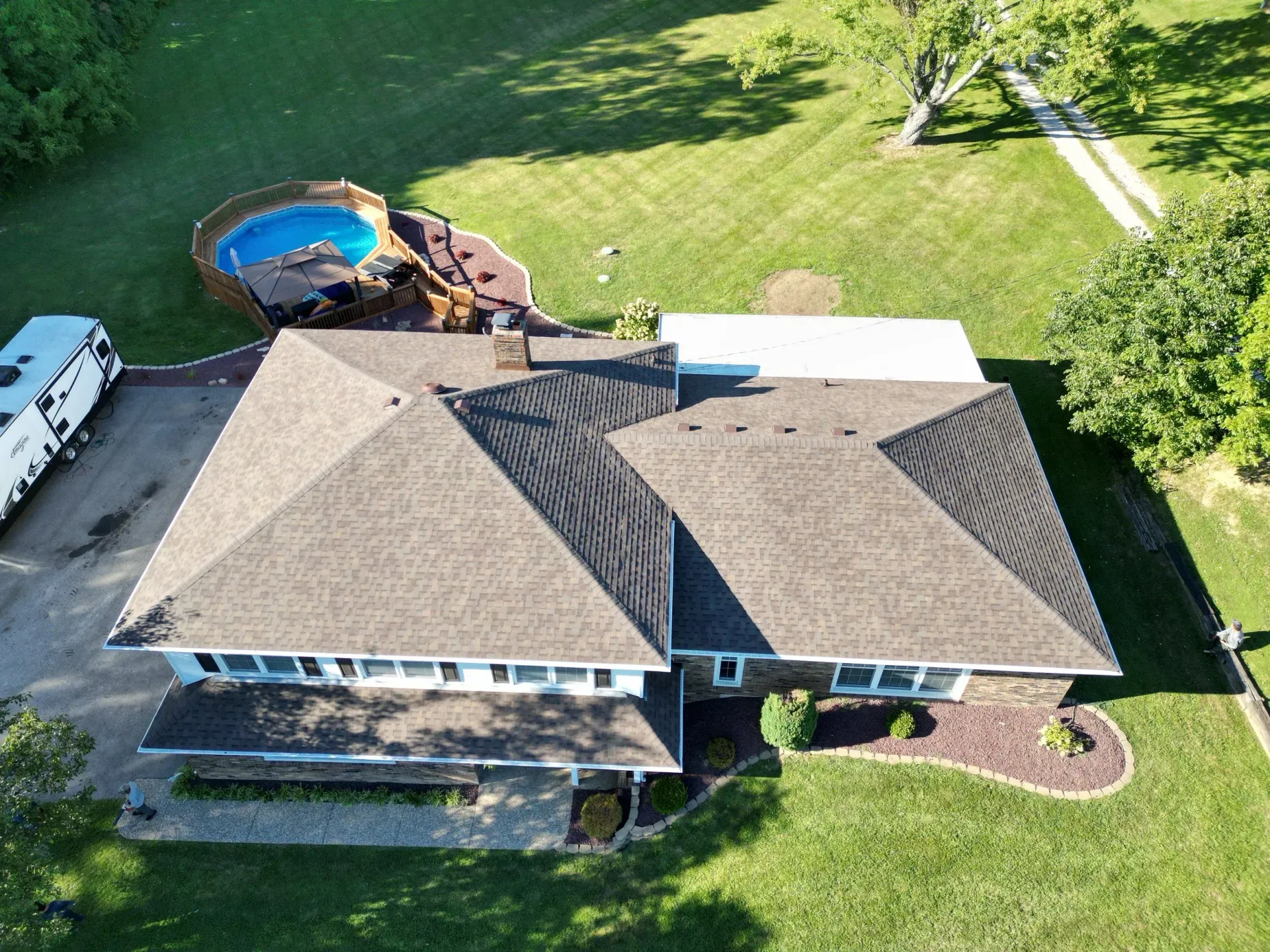 Aerial view of a house with a brown roof, backyard pool, and green lawn
