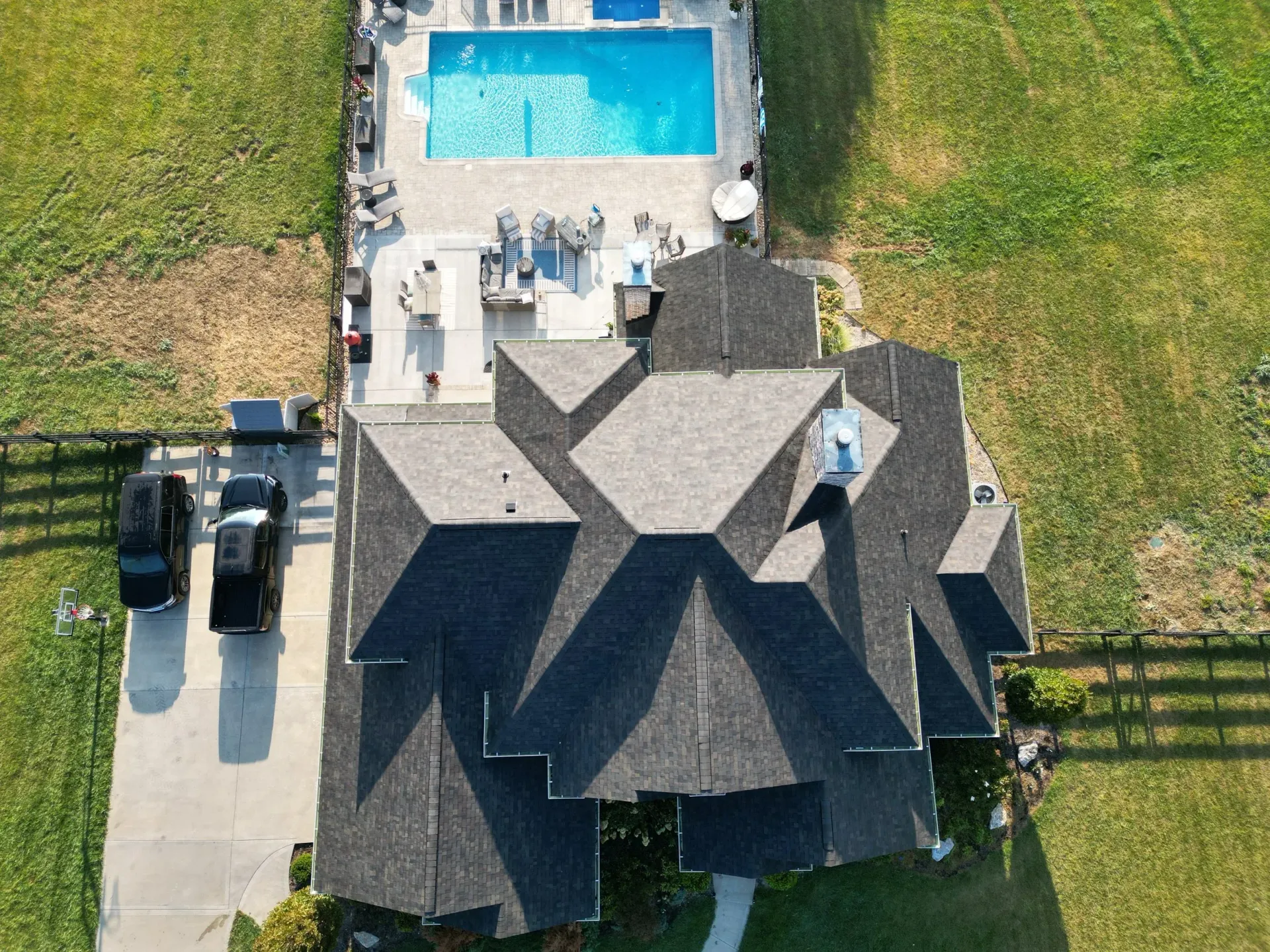 Aerial view of a house with a gray roof, driveway, and backyard swimming pool
