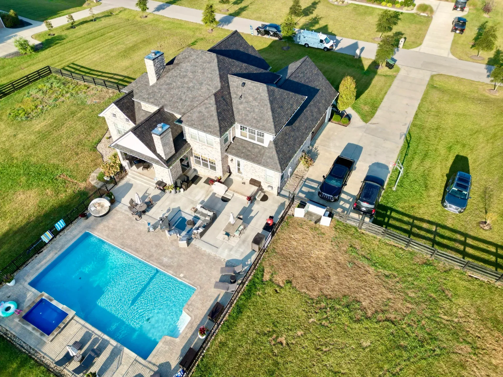 Aerial view of a large house with a blue backyard pool, patio furniture, and fenced green lawn