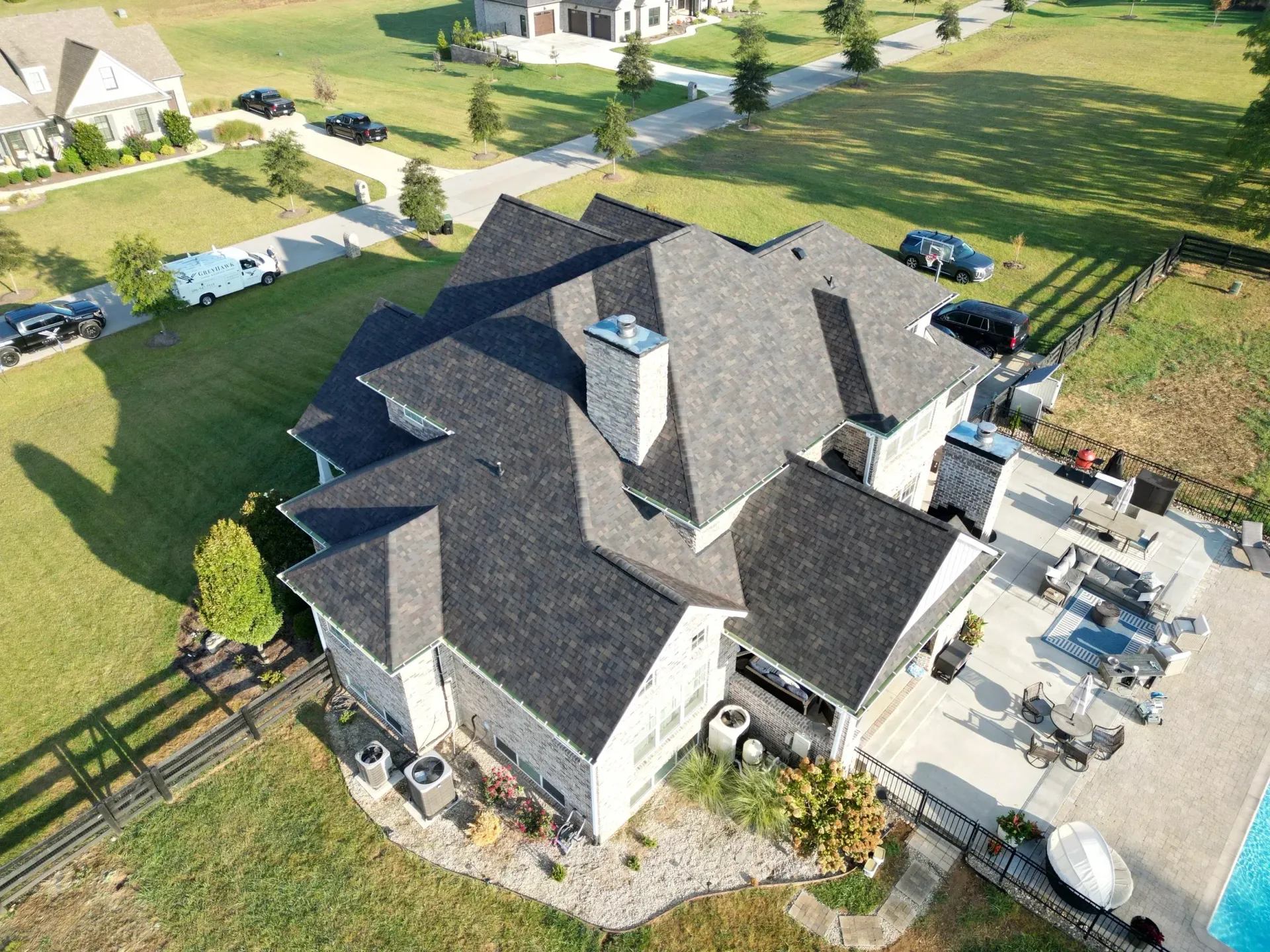 Aerial view of a large gray-roofed house with a driveway, patio, and surrounding lawn