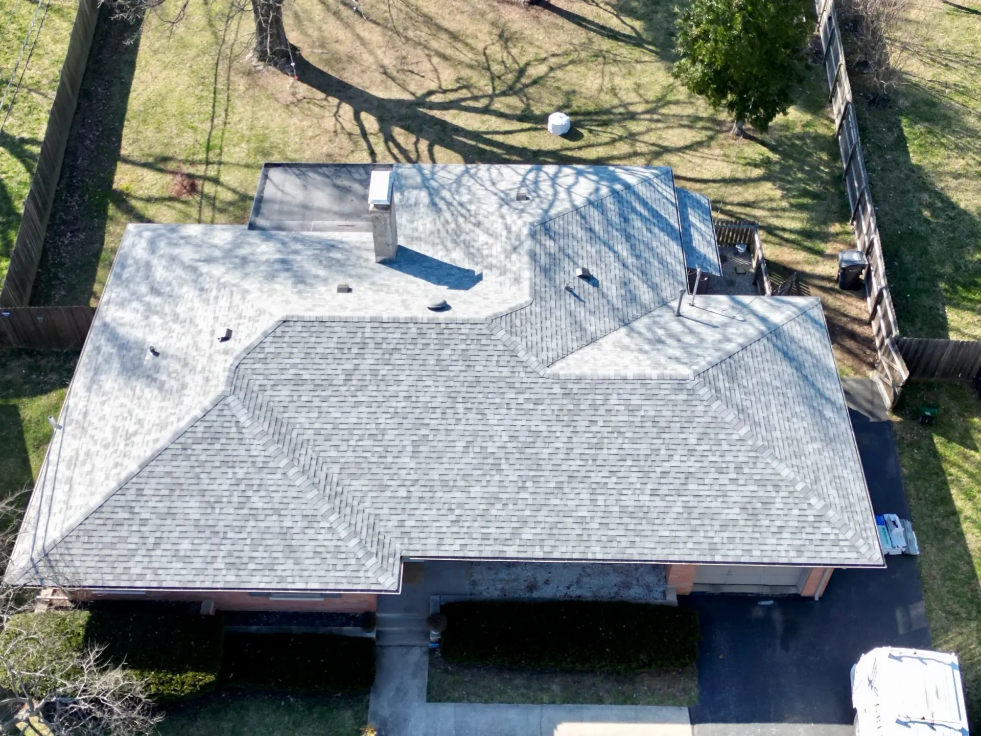 Aerial view of a gray-shingled house roof with trees and a driveway around it.