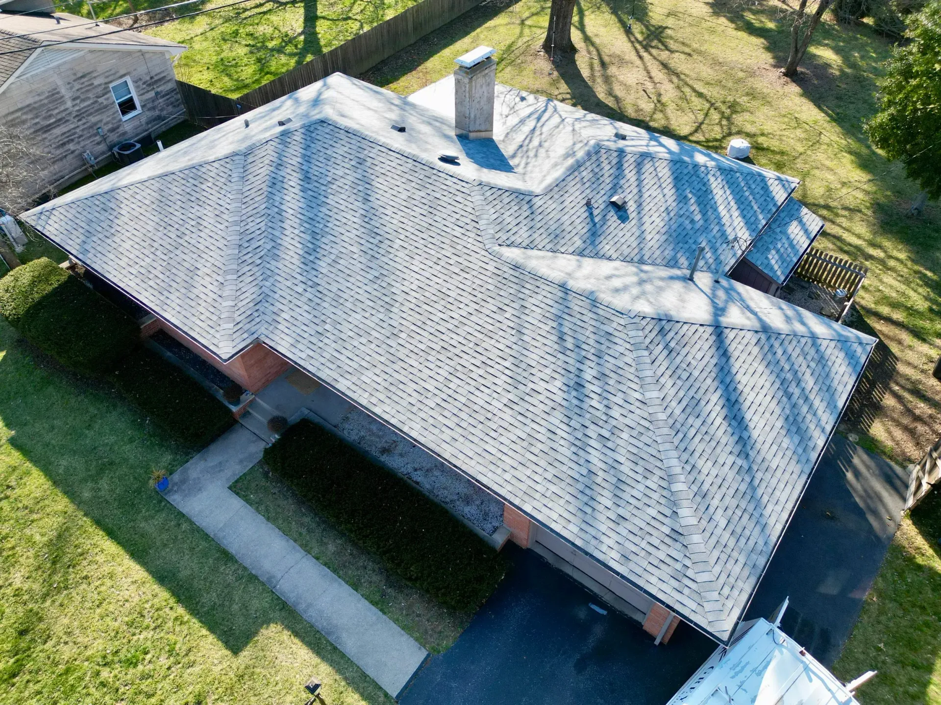 Aerial view of a gray shingled house with a covered porch and surrounding green lawn.