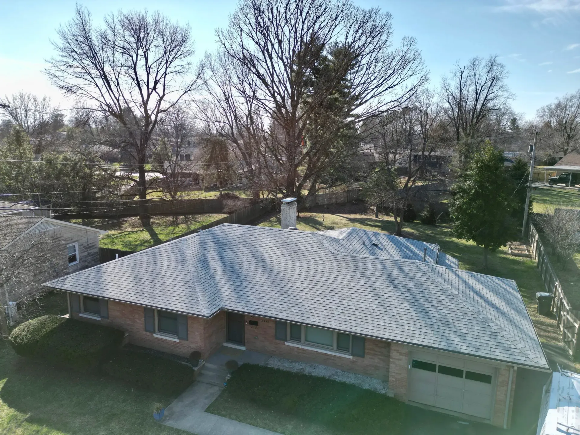 Single-story brick house with a light roof, surrounded by trees and a green yard on a sunny day