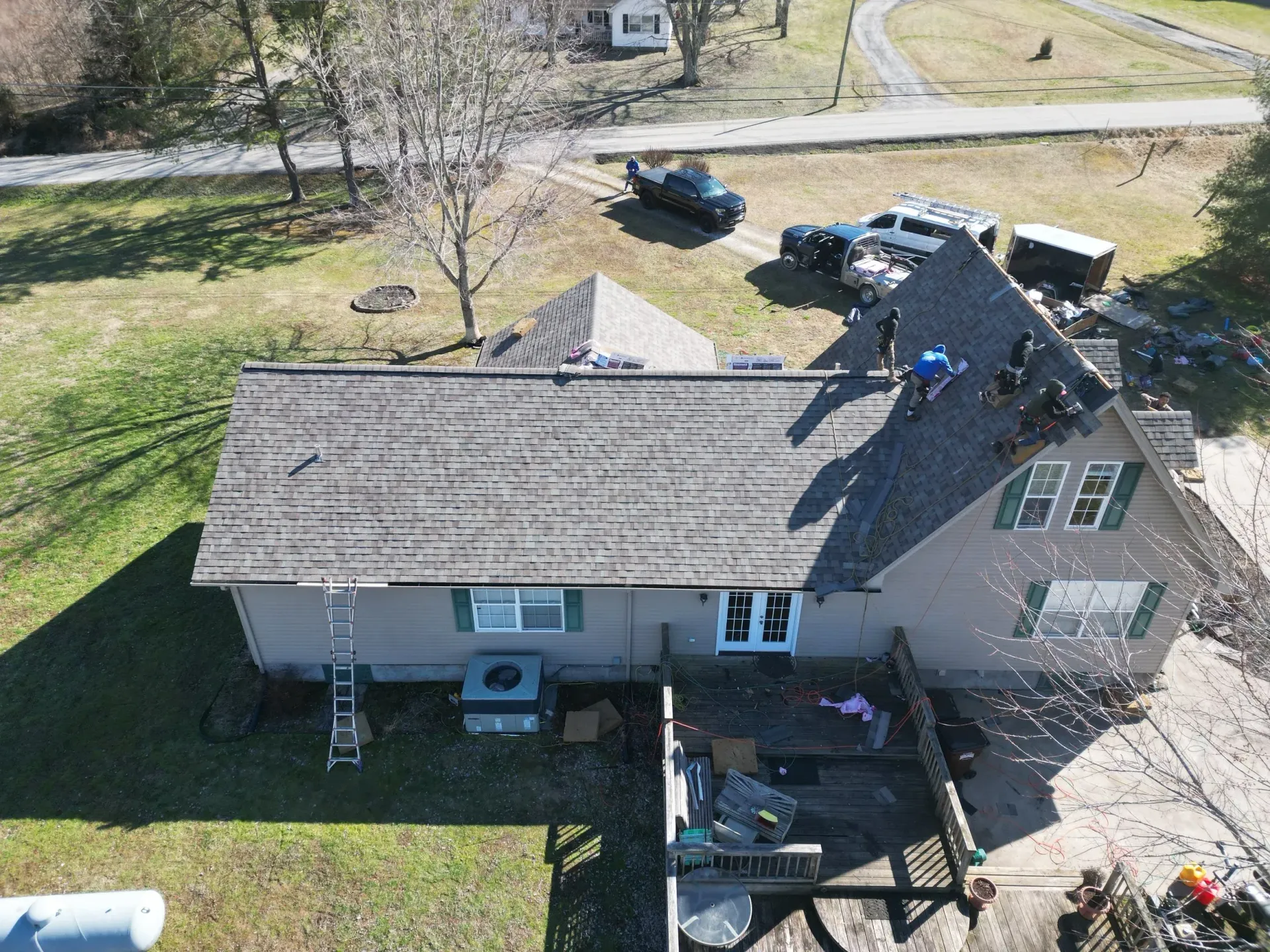 Aerial view of a house with a damaged roof, parked car, and yard in a rural setting
