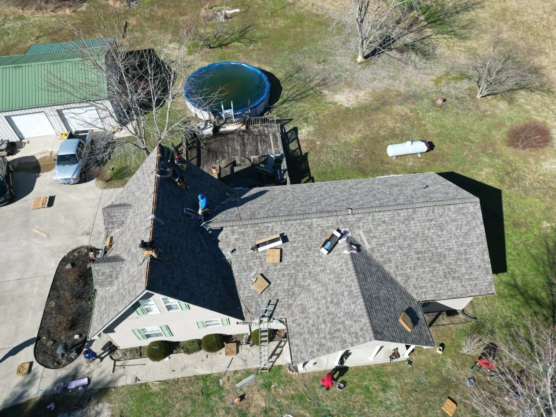 Aerial view of a house with a gray roof, backyard trampoline, and scattered items on the lawn.