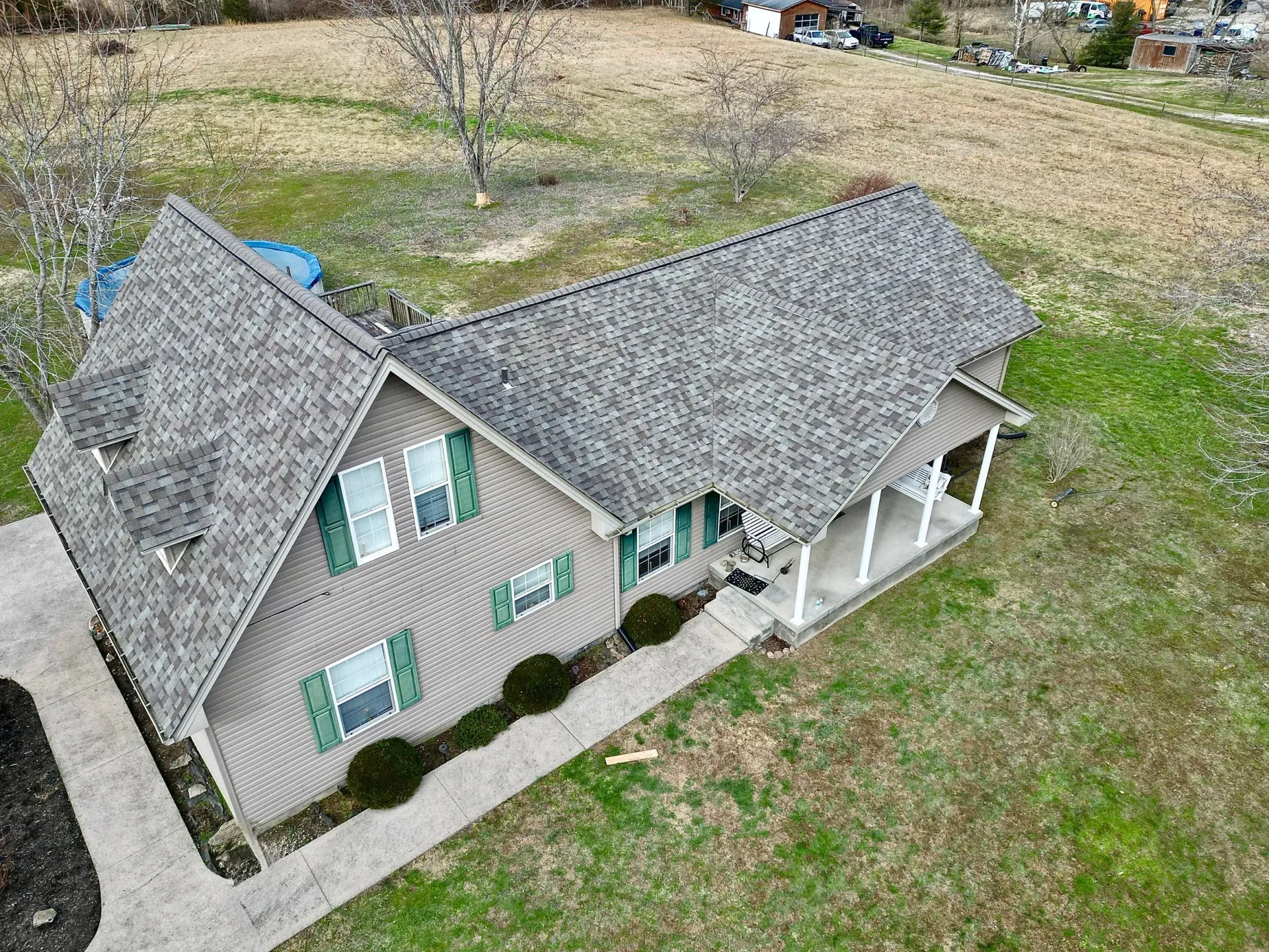 Small gray house with green shutters and a white porch, seen from an elevated angle in a grassy yard.